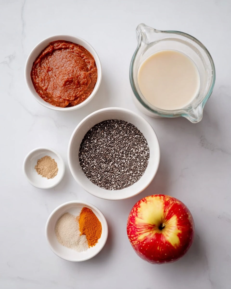 The image shows five containers with ingredients placed on a white marbled surface. In the center, there is a white bowl filled with small, black and white chia seeds. To the top right of the bowl is a clear glass pitcher with light cream-colored liquid. Below the pitcher is a red and yellow apple with a shiny skin. To the top left of the chia seeds, there is a white bowl containing a reddish-brown paste with smooth texture. Below this bowl, there is a smaller white bowl holding three spices with different shades – one orange, one beige, and one white grainy powder. The arrangement is simple and neatly spaced. Photo taken with an iphone --ar 4:5 --v 7