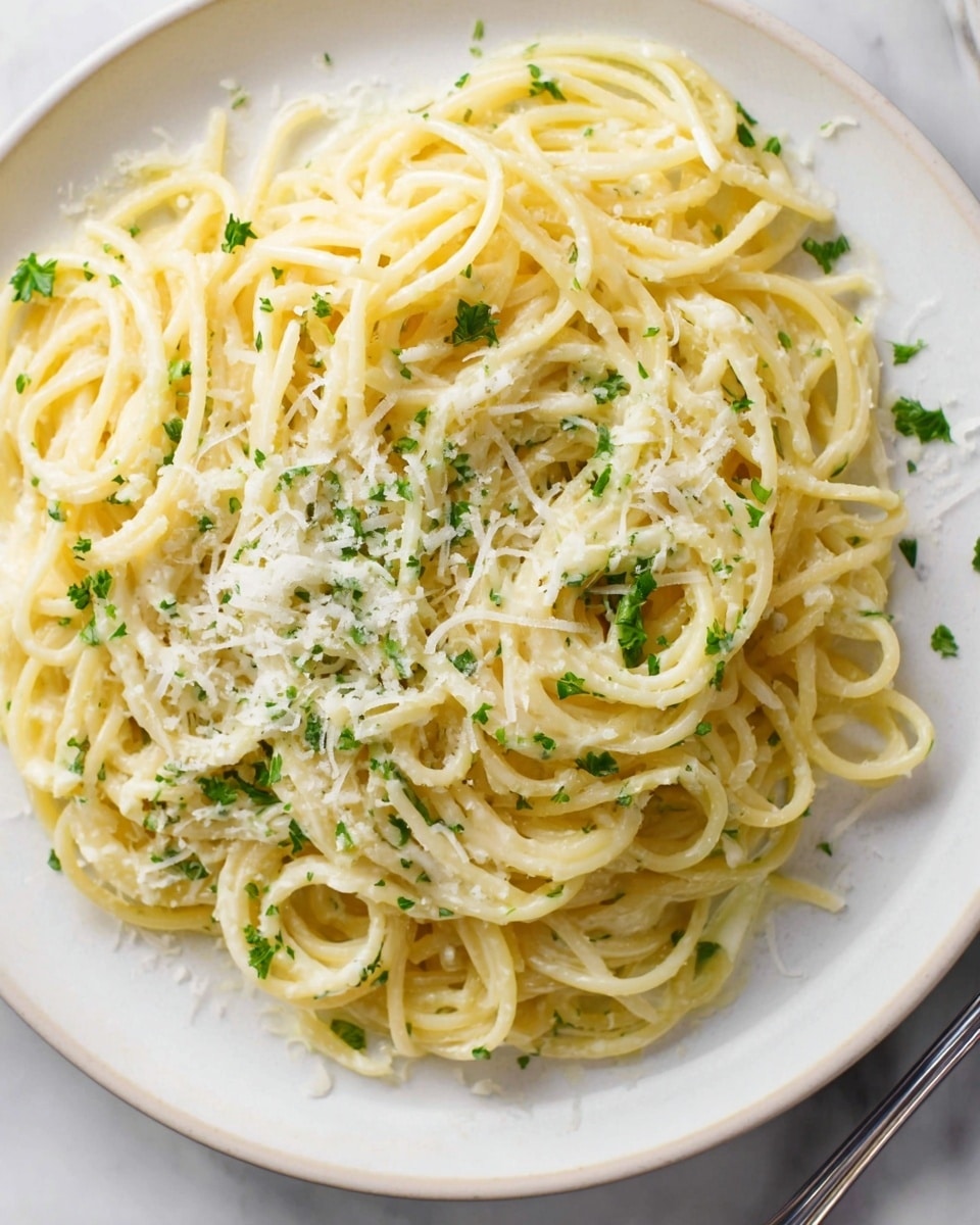 The image shows a close-up of a white plate filled with a single layer of spaghetti pasta covered in a light creamy sauce. The pasta is slightly twisted and mixed, with small green parsley pieces sprinkled throughout. There is a fine layer of shredded cheese on top, mainly in the middle, adding a soft texture. The plate is placed on a white marbled surface, and a small part of a fork is visible at the bottom right corner. The lighting is bright, highlighting the creamy sauce and the fresh herbs. photo taken with an iphone --ar 4:5 --v 7