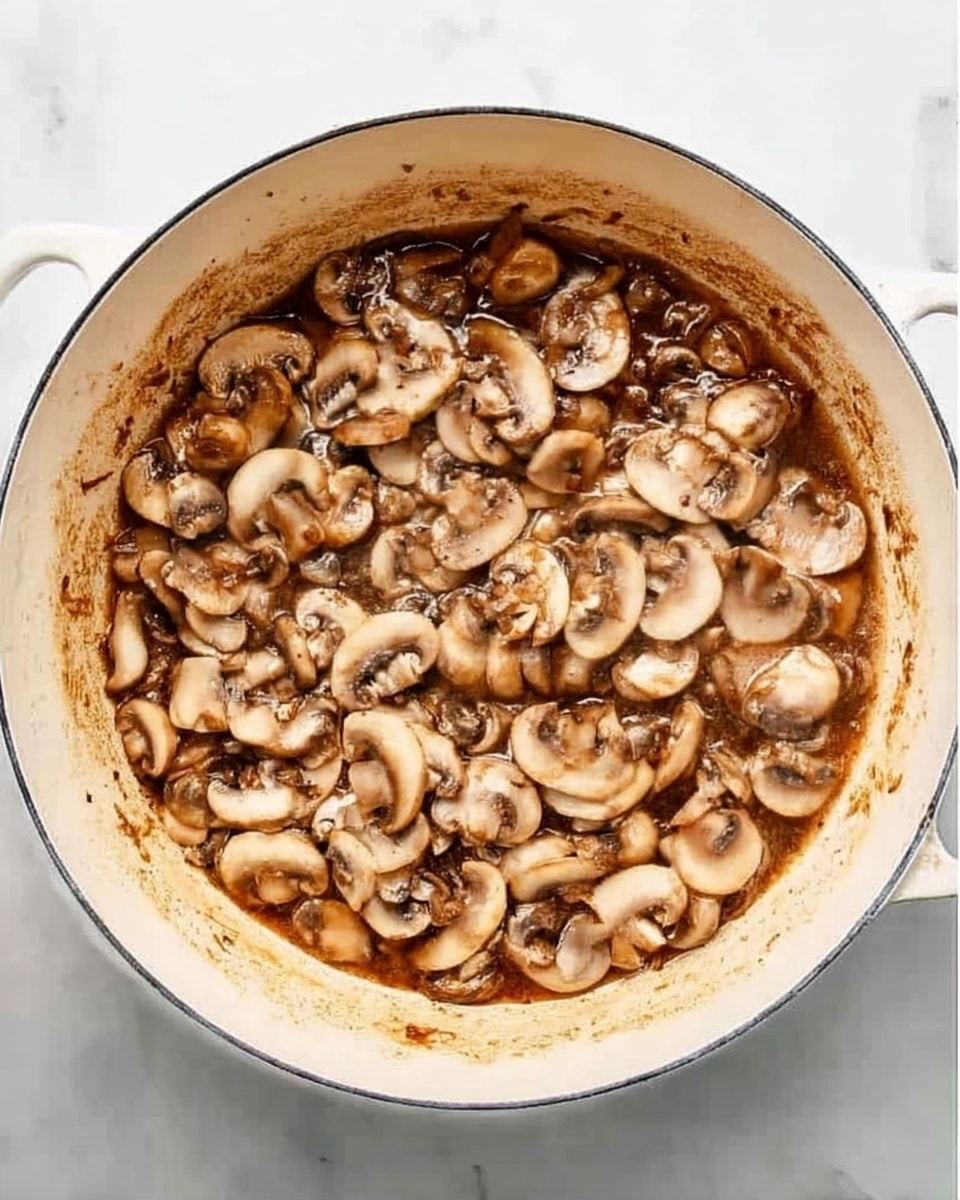 A round white pot filled with a mixture of sliced mushrooms cooking in a brown sauce. The mushrooms vary in size, are soft and slightly shiny, and cover the entire surface inside the pot. The pot sits on a white marbled surface, showing some browned marks around the inside edge where the sauce has cooked. Photo taken with an iphone --ar 4:5 --v 7
