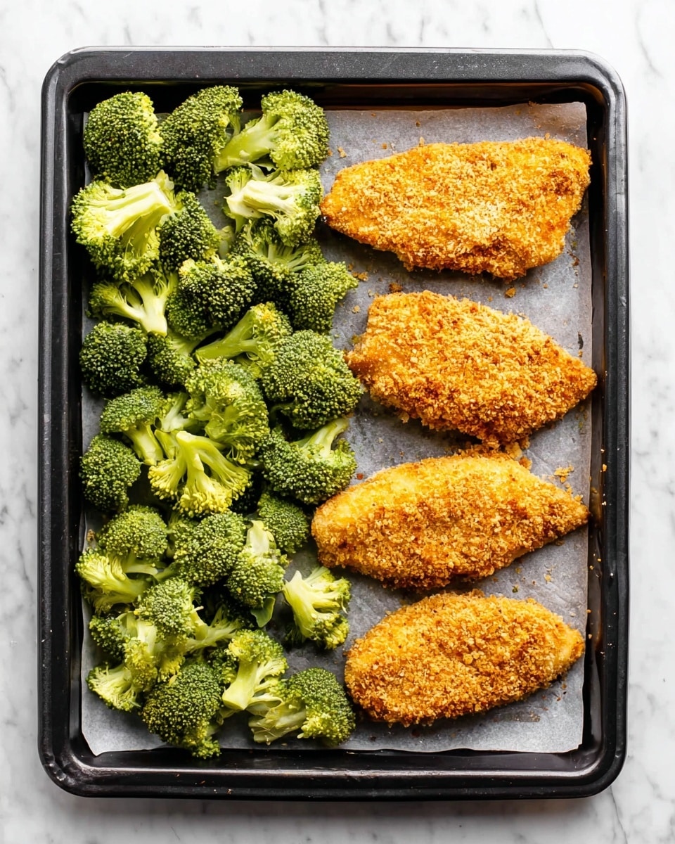 A black baking tray holds a layer of fresh broccoli florets on the left side, showing a vibrant green color with a slightly bumpy texture. On the right side, there are three pieces of breaded chicken with a golden-brown, crumbly coating, evenly spaced on a sheet of parchment paper that covers the tray. The tray is placed on a white marbled surface. photo taken with an iphone --ar 4:5 --v 7