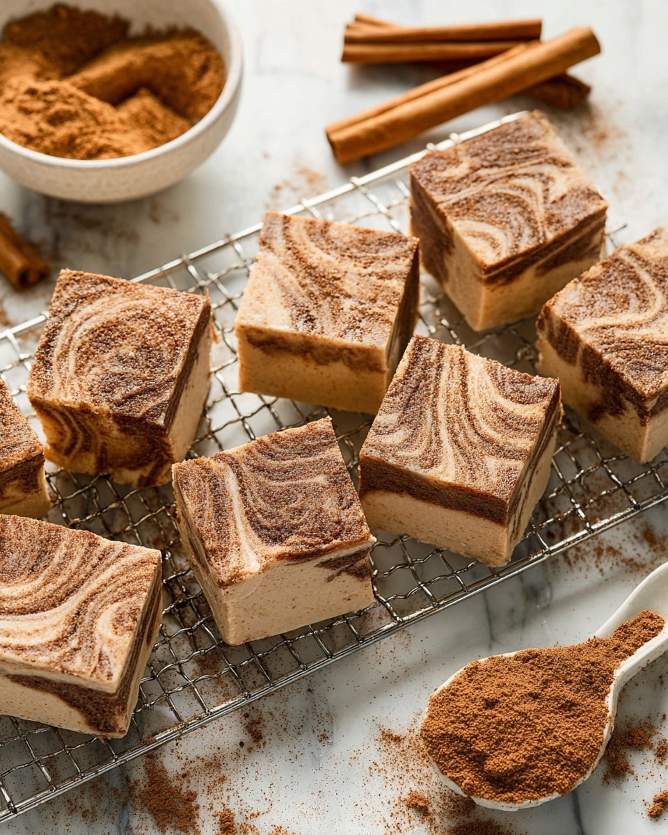 Several square pieces of cinnamon fudge rest on a metal cooling rack over a white marbled surface. Each piece has two visible layers: a bottom creamy beige layer and a top swirled layer with darker cinnamon brown patterns, dusted lightly with cinnamon powder. The fudge squares have smooth textures with clear, sharp edges. Nearby on the white marbled surface, a white bowl filled with cinnamon sugar and some cinnamon sticks are placed for decoration. The overall look is warm and inviting, with the cinnamon swirls creating a textured, natural pattern on the top of each fudge piece. Photo taken with an iphone --ar 4:5 --v 7