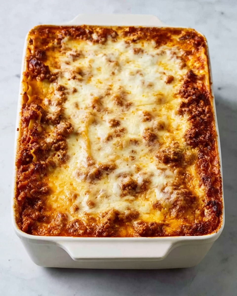 A white rectangular baking dish filled with a thick layered dish. The bottom layer is a rich dark red sauce with visible chunks of browned meat. Above that, there are several layers of soft pasta sheets, separated by layers of meat sauce and melted cheese. The top layer is covered with melted golden cheese, slightly browned and bubbly, creating a textured surface with some browned spots. The dish sits on a white marbled surface. photo taken with an iphone --ar 4:5 --v 7