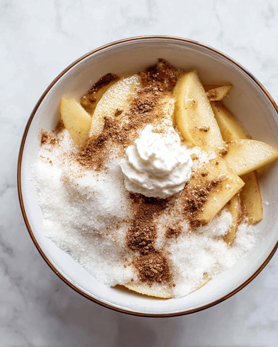 A bowl filled with thin slices of pale yellow apples at the bottom, covered with a thick layer of white granulated sugar. On top of the sugar, there is a sprinkle of light brown cinnamon powder unevenly spread. In the middle of the bowl, a small dollop of smooth, white whipped cream sits prominently. The bowl is white with a thin, brown rim, placed on a white marbled surface. photo taken with an iphone --ar 4:5 --v 7