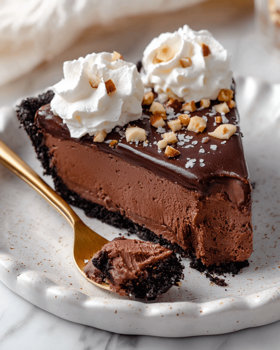 A single slice of rich chocolate pie is shown on a white speckled plate with a scalloped edge, placed on a white marbled surface. The pie has three layers: a dark, crumbly chocolate crust at the bottom, a thick, smooth chocolate mousse filling in the middle, and a glossy dark chocolate ganache layer on top sprinkled with small chunks of nuts and coarse salt. Two large swirls of white whipped cream sit on one side of the slice, adding contrast. A gold fork resting on the plate holds a bite of the pie, showing the creamy texture of the mousse inside photo taken with an iphone --ar 4:5 --v 7