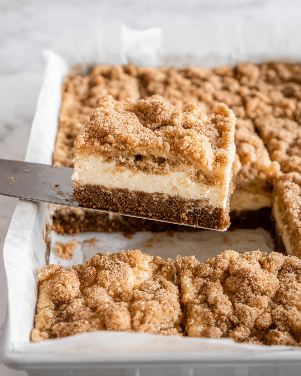 The image shows a layered dessert bar cut into square pieces, with one piece lifted on a metal spatula. The dessert has three distinct layers: a dark brown crumbly base, a thick middle layer of creamy white filling, and a top layer of golden brown crumbly streusel with visible small chunks and a sprinkle of cinnamon or sugar. The dessert is in a white pan lined with white parchment paper, set on a white marbled surface. The texture of the top layer looks crunchy and uneven, the middle is smooth and creamy, and the base is firm and crumbly. Photo taken with an iphone --ar 4:5 --v 7
