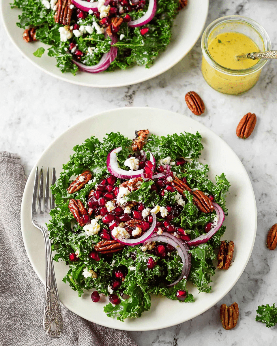 Two white plates rest on a white marbled surface, each filled with a fresh kale salad. The salad has three clear layers: the base layer is dark green kale with a bumpy texture, the middle layer includes thin, curved slices of bright purple onion, and the top layer is scattered with whole brown pecans, small white crumbled cheese, and shiny red pomegranate seeds. A silver fork lies on the front plate's left side, partially resting on the salad. To the right, a clear jar with yellow salad dressing and a spoon inside is visible, with a few pecans and green leaves scattered on the surface around the plates. Photo taken with an iphone --ar 4:5 --v 7