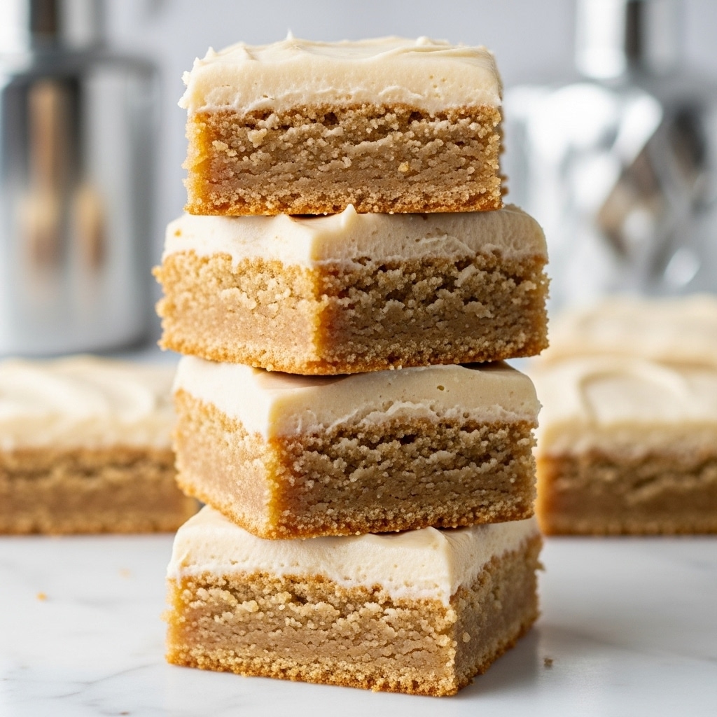 The image shows small square bars stacked, each bar has two layers: a thick brown textured bottom layer that looks soft and cake-like, and a smooth pale beige creamy layer on top. The bars rest on a white cloth with a clean white marbled background. The creamy top looks slightly cracked and matte, while the bottom appears soft and moist. Photo taken with an iphone --ar 4:5 --v 7