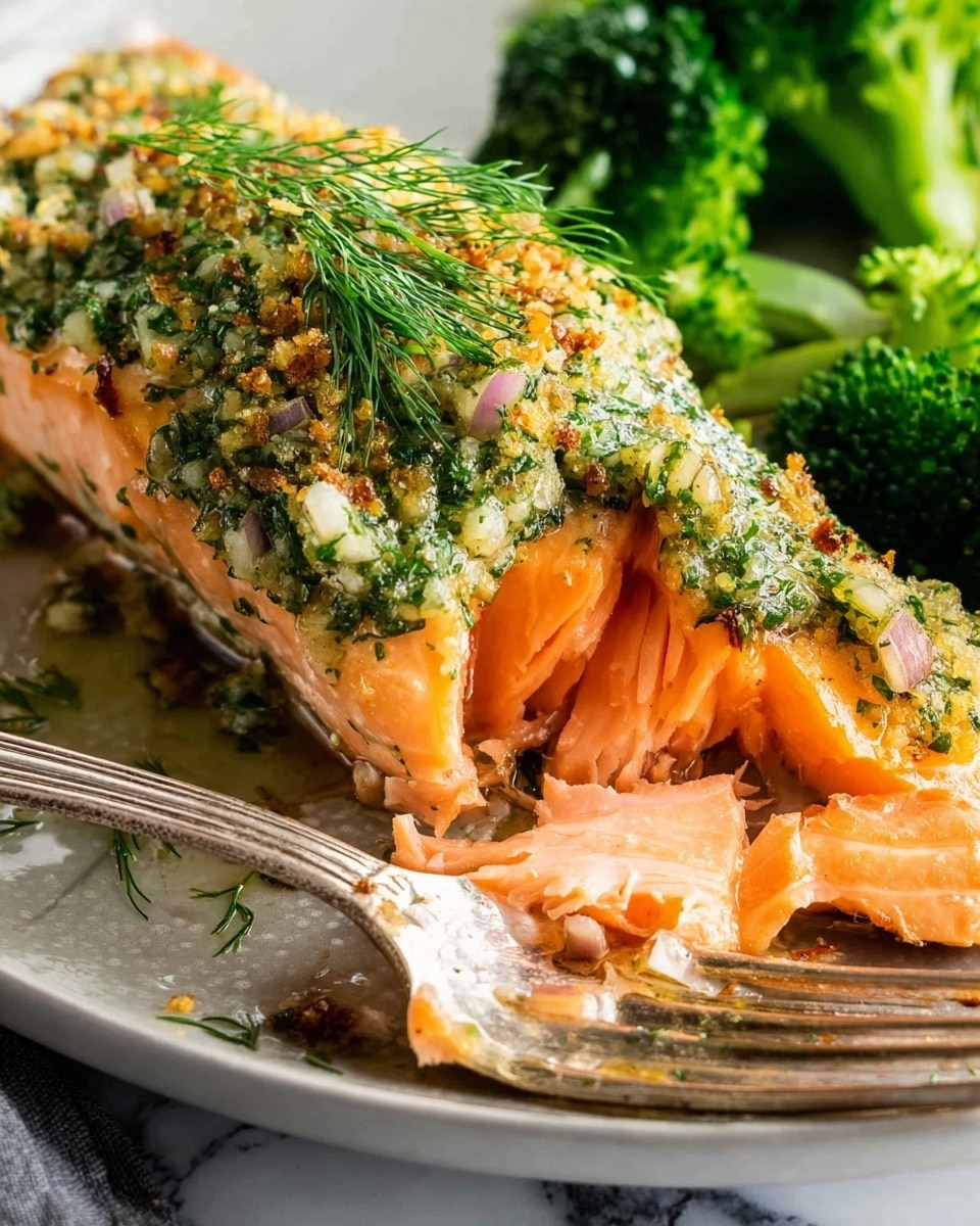 A close-up view of a cooked salmon fillet topped with a green herb sauce mixed with small pink bits and sprinkled with golden brown crumbs, with visible fresh dill sprigs on top; the salmon's bright orange flesh is sliced, showing its tender, flaky texture beneath the sauce. The fillet rests on a vintage silver fork, placed on a white plate with a slightly wet surface which reflects light. To the right side of the plate, there are bright green steamed broccoli florets with a fresh, bumpy texture. The background is a white marbled texture. Photo taken with an iphone --ar 4:5 --v 7