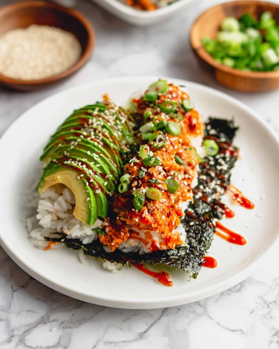 A white plate holds a layered dish starting with a dark green, almost black, seaweed sheet at the bottom. On top is a layer of white rice, partly visible, with a thick orange layer of spicy tuna mixed with sauce covering most of the rice. Sliced green avocado curves along the top left side, drizzled with red sauce, and the dish is sprinkled generously with white sesame seeds and chopped green onions. The plate sits on a white marbled surface with a small wooden bowl of green onion slices and another bowl of white sesame seeds visible in the blurred background. Photo taken with an iphone --ar 4:5 --v 7