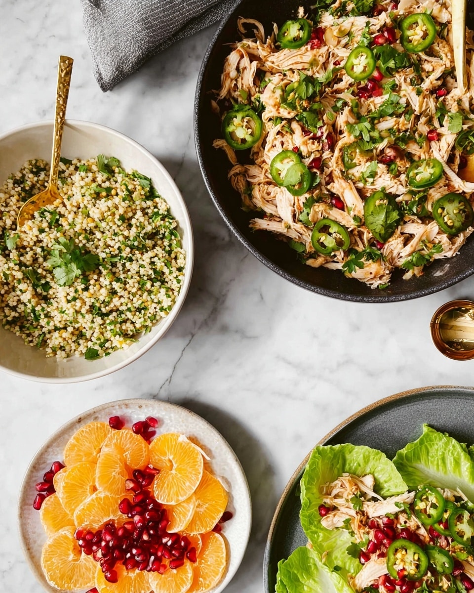 A black pan filled with shredded cooked chicken mixed with green sliced peppers and topped with sliced green jalapeños sits on a white marbled surface. Next to it is a white bowl of small pearl couscous mixed with chopped green herbs with a gold spoon resting inside. Nearby, a white plate holds thin round slices of orange and pale fruit, scattered with bright red pomegranate seeds and a gold spoon. Above this plate, a gray plate contains a fresh green lettuce leaf topped with more shredded chicken, sliced green jalapeños, and sprinkled with pomegranate seeds. A lettuce head sits partially visible in the bottom right corner. photo taken with an iphone --ar 4:5 --v 7