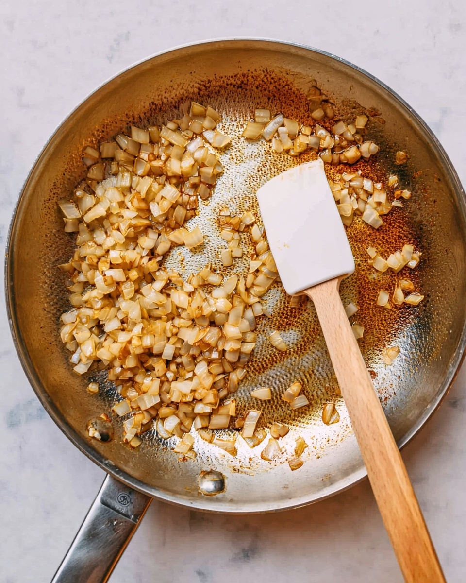 A shiny metal frying pan filled with small, light brown cooked onion pieces spread around the edges, leaving a clean center that shows brown cooked marks on the pan's surface. In the center, there is a white spatula with a wooden handle resting flat, touching the onions. The pan is placed on a white marbled surface. photo taken with an iphone --ar 4:5 --v 7