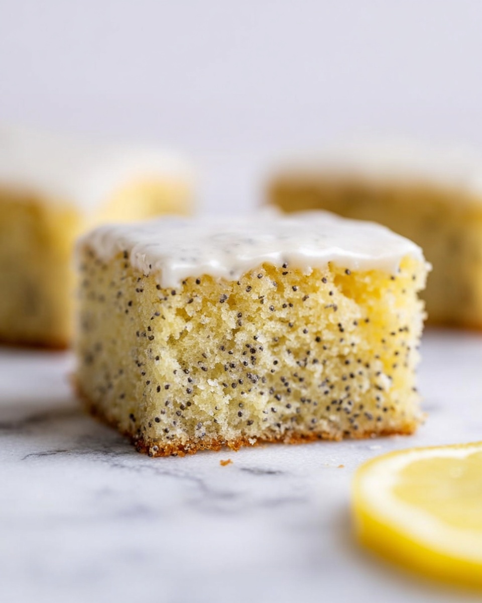 A close-up of a square piece of lemon poppy seed cake with two visible layers: the bottom layer is a light yellow, soft, and moist cake with tiny black poppy seeds evenly spread inside, showing a slightly crumbly texture; the top layer is a thin, smooth, glossy white icing, covering the cake completely. The cake sits on a white marbled surface with a blurred slice of lemon in the foreground and two other pieces of the same cake blurred in the background. Photo taken with an iphone --ar 4:5 --v 7