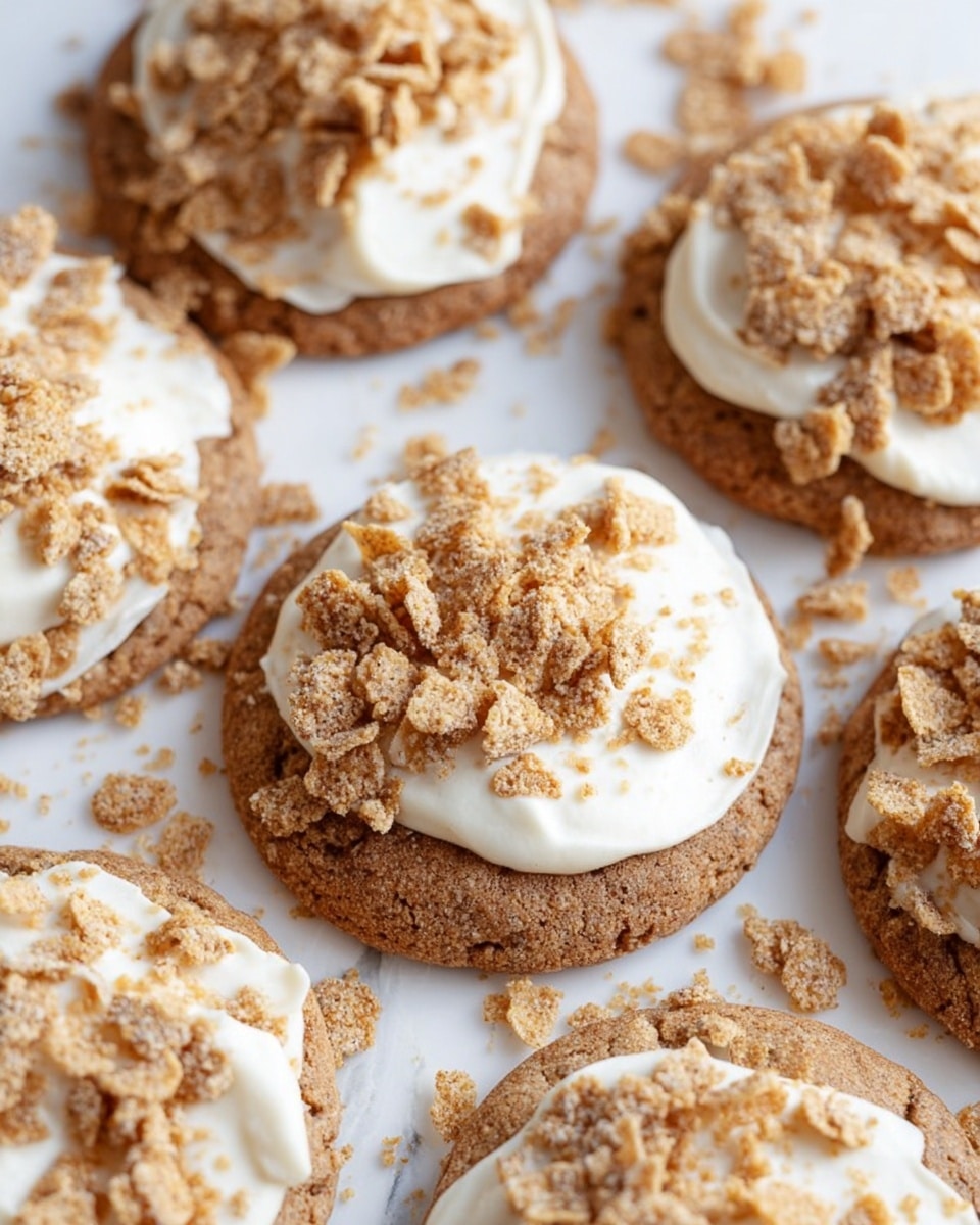 The image shows several round cookies placed together on a white marbled surface. Each cookie has one thick brown base layer that looks soft and speckled, topped with a layer of creamy white frosting that is unevenly spread. On top of the frosting, there is a crumbly layer of crushed light brown cereal pieces scattered generously, with some crumbs also lying around the cookies on the surface photo taken with an iphone --ar 4:5 --v 7