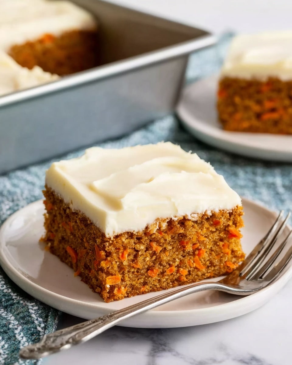A square piece of carrot cake with two layers is placed on a white plate; the bottom layer is a moist, orange-brown cake with visible small bits of carrot, and the top layer is thick, creamy white frosting spread smoothly with soft peaks. A silver fork rests on the plate beside the cake. In the background, another plate with a similar piece of cake and a silver baking pan partially filled with carrot cake are visible on a white marbled surface. Photo taken with an iphone --ar 4:5 --v 7