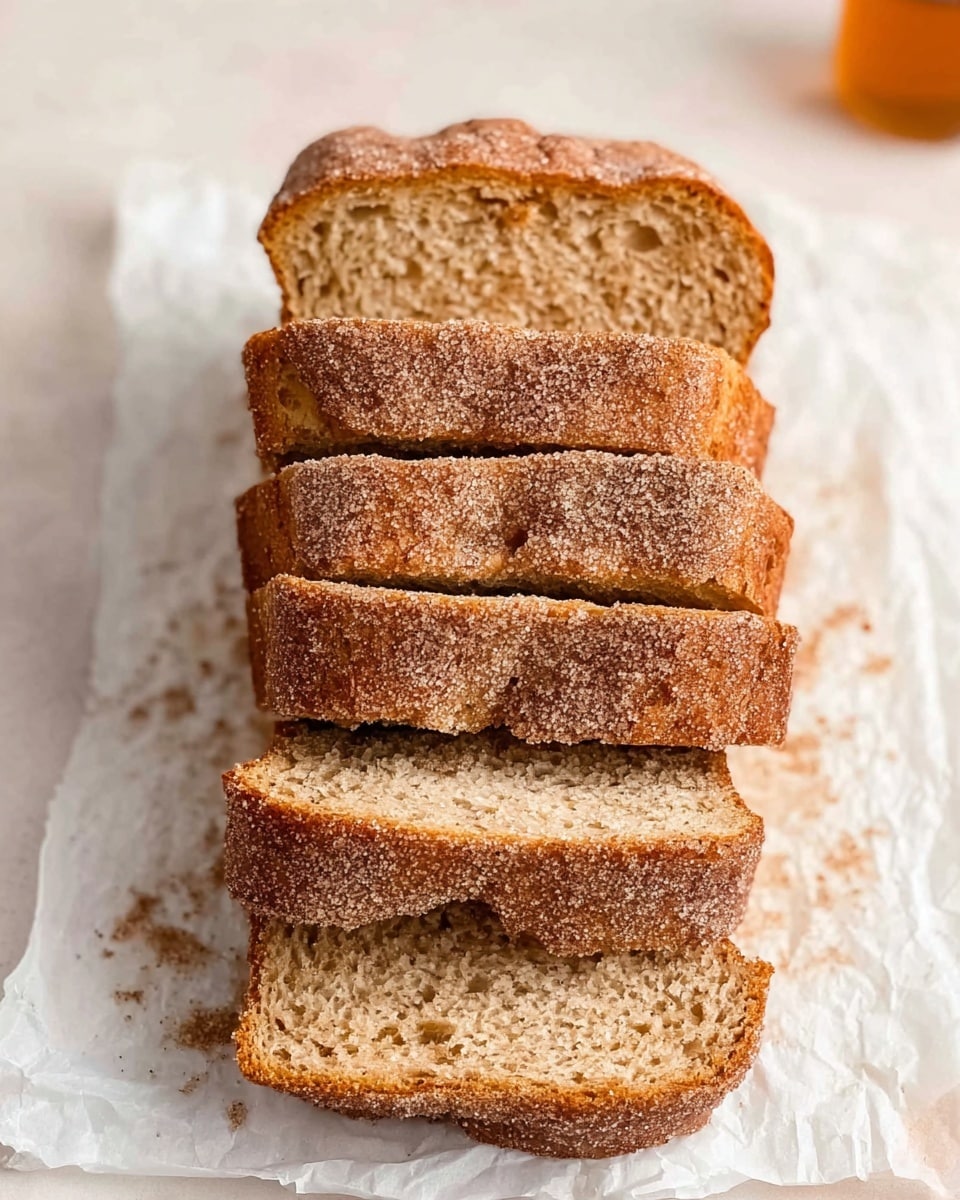 The image shows seven slices of cinnamon sugar bread stacked neatly on a piece of white parchment paper. The bread has a light golden brown crust dusted generously with cinnamon sugar crystals, giving it a slightly rough texture on top. Inside, the bread looks soft and moist with a slightly dense crumb and specks of cinnamon scattered throughout. The slices are arranged on a white marbled surface with a soft natural light coming from the top right corner. The scene feels warm and inviting, with no additional props visible. Photo taken with an iphone --ar 4:5 --v 7
