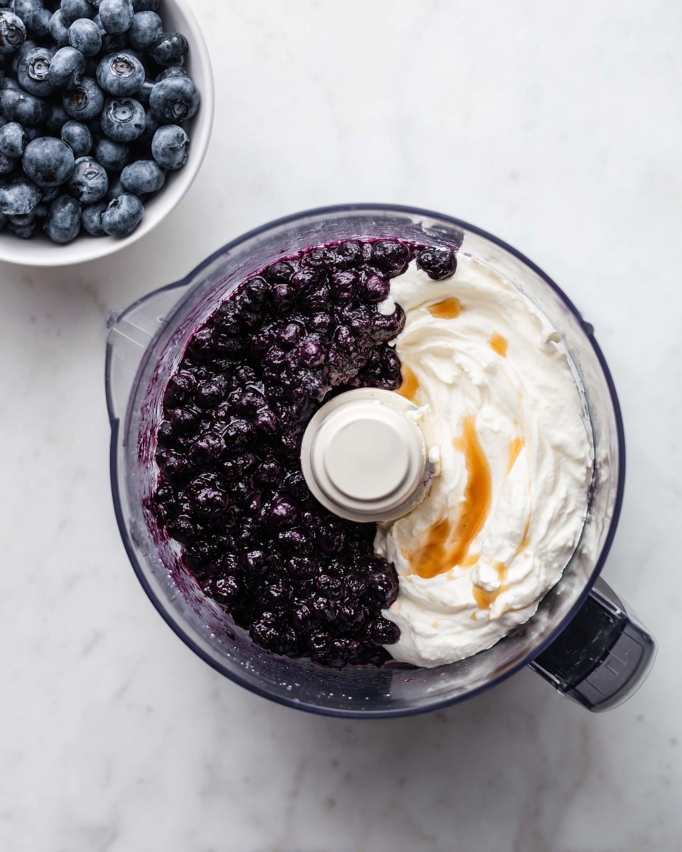 A top view of a clear food processor bowl filled with two main layers: on the left side, a large layer of dark purple frozen blueberries, and on the right side, a thick layer of white creamy yogurt mixed with some light brown honey drizzled on top. The bowl is placed on a white marbled surface with a white bowl of more frozen blueberries in the top left corner. photo taken with an iphone --ar 4:5 --v 7