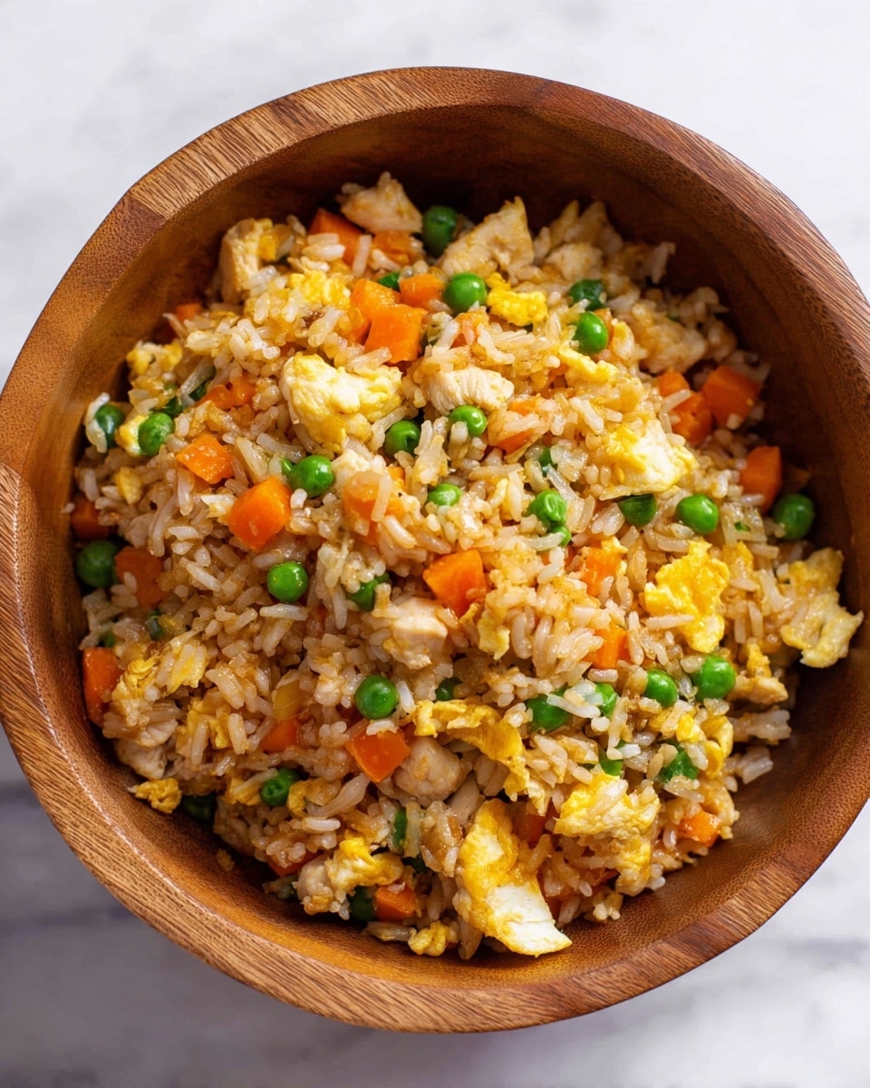 A wooden bowl filled with fried rice that has a mix of four main layers: the base layer is light brown rice grains, scattered with bright green peas and small, diced orange carrot pieces; the next layer shows soft, chopped white chicken pieces mixed evenly; on top of that, there are fluffy yellow scrambled egg bits that add color and texture throughout; the whole dish looks warm and fresh, set against a white marbled surface. photo taken with an iphone --ar 4:5 --v 7