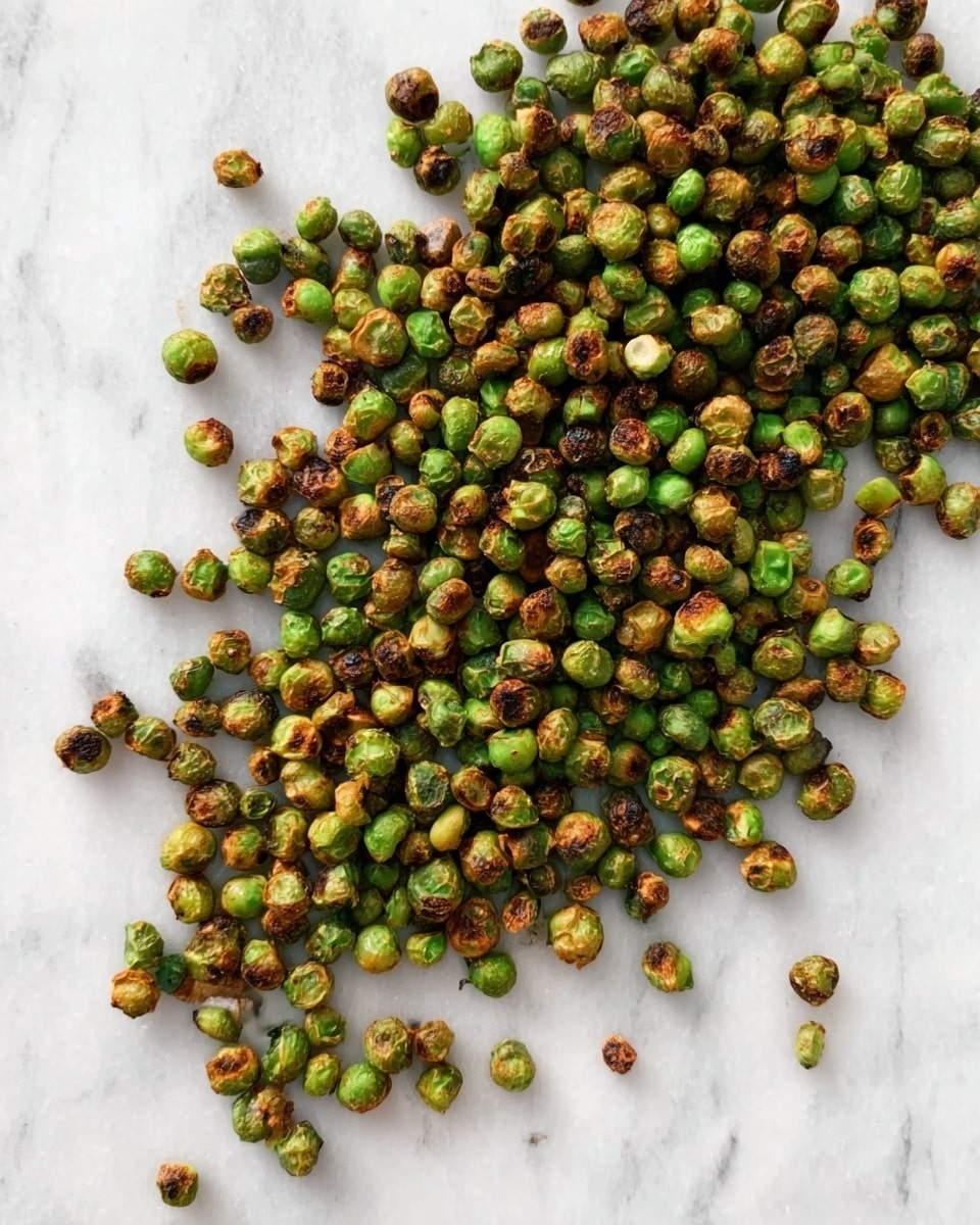 The image shows many small roasted green peas spread out unevenly on a white marbled surface. The peas have a crispy texture with parts that are darker brown, indicating they are well roasted, and some are brighter green. The peas vary slightly in size and are scattered randomly across the white marbled surface. photo taken with an iphone --ar 4:5 --v 7