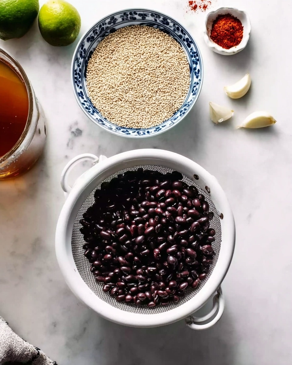 The image shows a white colander filled with small, shiny black beans placed on a white marbled surface. Above and slightly to the left is a white bowl with a blue patterned rim filled with pale beige quinoa grains. To the right of the bowl, there are three cloves of garlic on the surface. Near the top edge, a small white dish holds a red spice powder. On the left side, a clear glass container holds a brown liquid, likely broth or stock. A pair of lime wedges rests on the top left corner, partially visible. The whole setup is clean and organized, with all items placed neatly on the white marbled background photo taken with an iphone --ar 4:5 --v 7