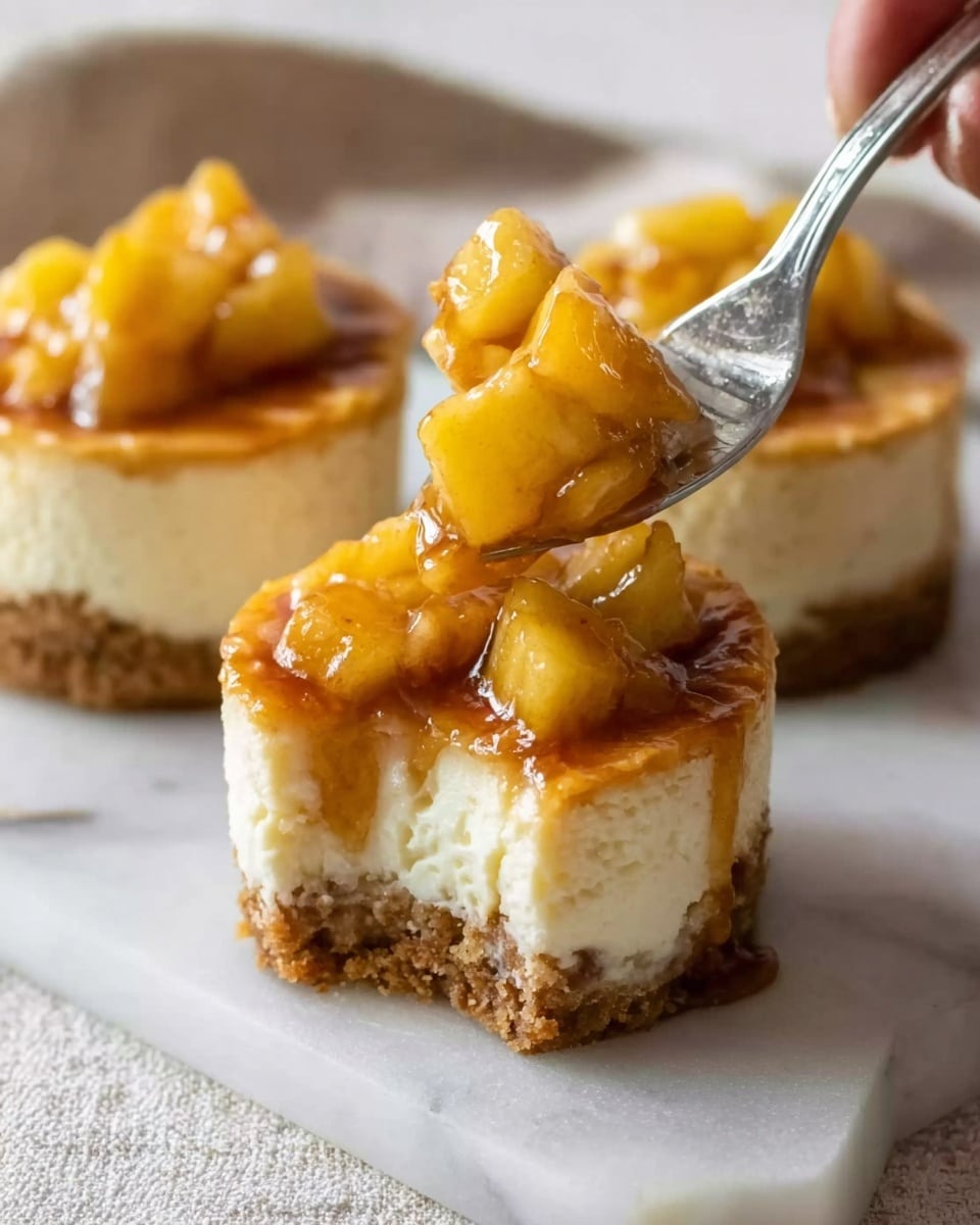 The image shows three small cheesecake cups on a white marbled surface. Each cheesecake has three layers: a crumbly golden brown base at the bottom, a thick creamy white middle layer, and a glossy topping made of small yellow apple pieces covered in a shiny caramel sauce. One cheesecake in the front has a piece taken out, held by a silver fork with a woman’s hand gently touching it. The apple topping looks soft and juicy with a syrup dripping down the sides, making the cheesecake look sweet and inviting. photo taken with an iphone --ar 4:5 --v 7