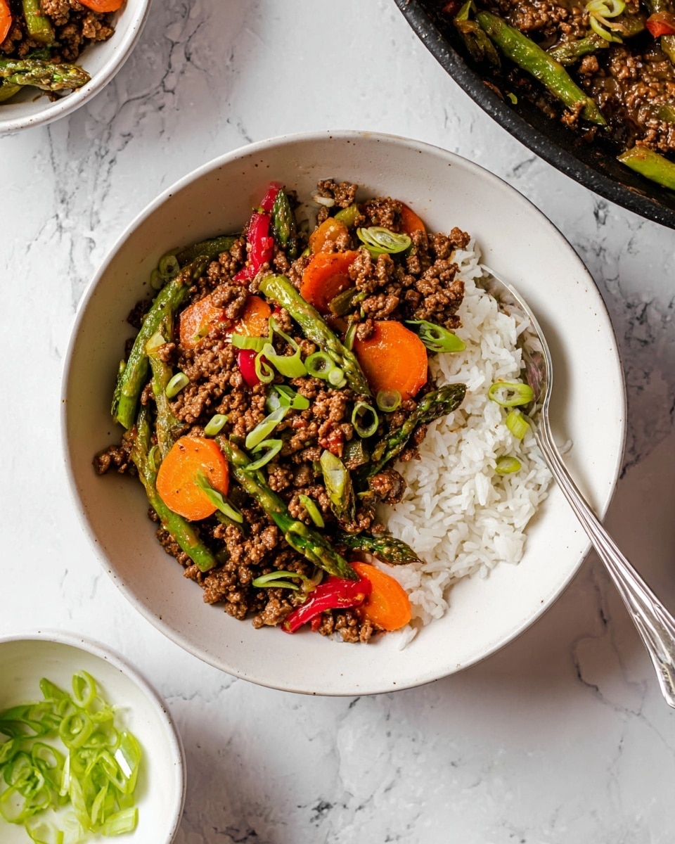 A white bowl filled with a two-layer dish is shown from above. The bottom layer is made of light, fluffy white rice on the right half of the bowl. The top layer covers the left half with a mix of ground meat cooked with green asparagus spears, round orange carrot slices, and small red bell pepper pieces. Thin slices of green onion are scattered on top, adding a fresh touch. A silver spoon leans inside the bowl on the right side. The bowl rests on a white marbled surface with a small white bowl containing sliced green onions and part of a black skillet with more cooked meat and vegetables nearby. Photo taken with an iphone --ar 4:5 --v 7