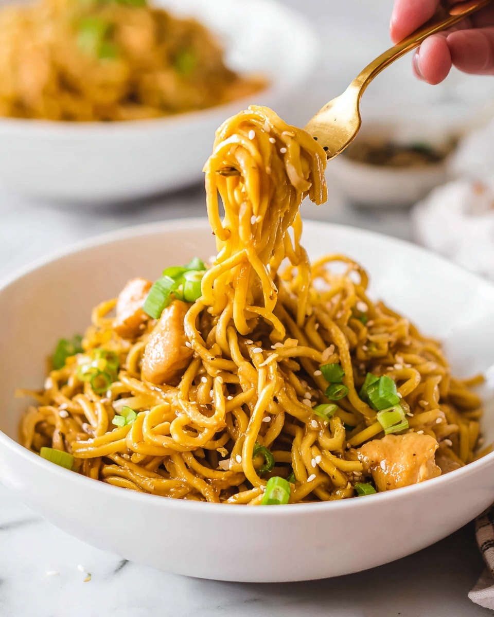 A white bowl filled with a heap of yellowish-brown noodles mixed with small light brown chicken pieces, garnished with small green onion slices and sesame seeds scattered on top. A golden fork held by a woman's hand lifts a twisted bundle of noodles and a chicken piece from the bowl, showing a close-up view of the tangled noodles and tender chicken beneath. The background is softly blurred with another bowl of noodles faintly visible, all set on a white marbled surface. photo taken with an iphone --ar 4:5 --v 7