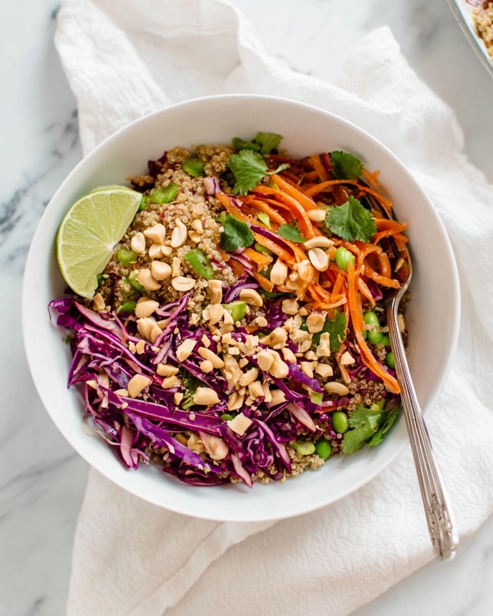 A white bowl holds a colorful quinoa salad with three main layers: at the bottom is a base of cooked quinoa grains in pale beige; the middle layer is a mix of thin purple cabbage strips, bright orange shredded carrots, and green snap peas cut into small pieces; the top layer includes chopped peanuts scattered all over, adding a crunchy texture, along with some fresh green cilantro leaves mixed in. On one side inside the bowl is a small wedge of light yellow lime. A silver spoon rests inside the bowl on the right. The bowl sits on a white marbled surface with a white cloth nearby. Photo taken with an iphone --ar 4:5 --v 7