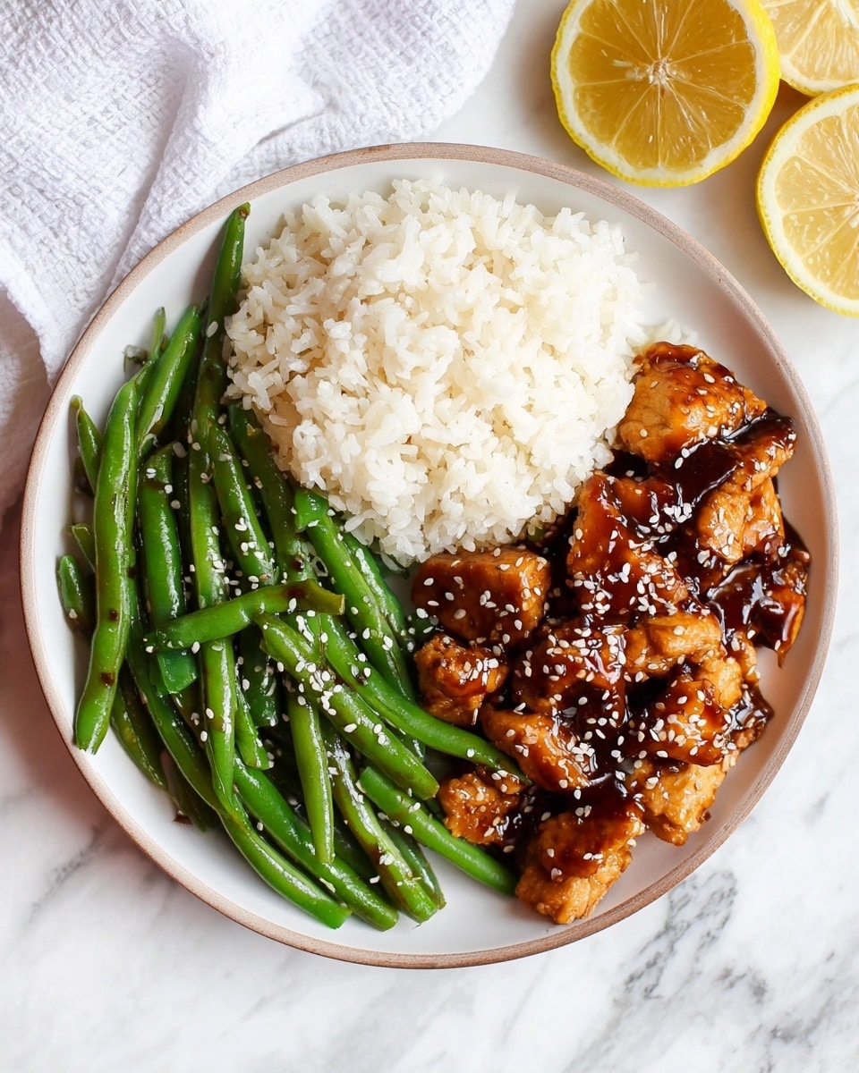 A round white plate holds three sections of food on a white marbled surface: the first section at the top left is a fluffy mound of white rice with a soft, grainy texture; to the right of the rice is a pile of bright green steamed green beans that are smooth and shiny, sprinkled with white sesame seeds; below the rice and green beans is a portion of golden brown chicken pieces coated in a glossy dark brown sauce, also topped with white sesame seeds. A white cloth napkin is partly visible at the top left, and two lemon halves are on the white marbled surface at the top right. Photo taken with an iphone --ar 4:5 --v 7
