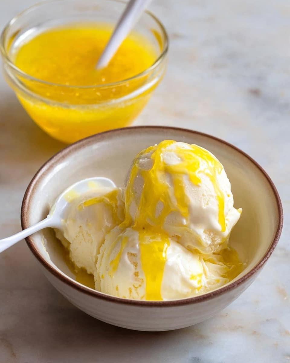 The image shows a white ceramic bowl with two scoops of creamy white ice cream inside. The ice cream is topped with a shiny, bright yellow sauce drizzled unevenly over it. A small white spoon with some sauce on it is resting inside the bowl on the left side. In the background, there is a clear glass bowl filled with the same yellow sauce with a white spoon inside it. The entire scene is placed on a white marbled surface. photo taken with an iphone --ar 4:5 --v 7