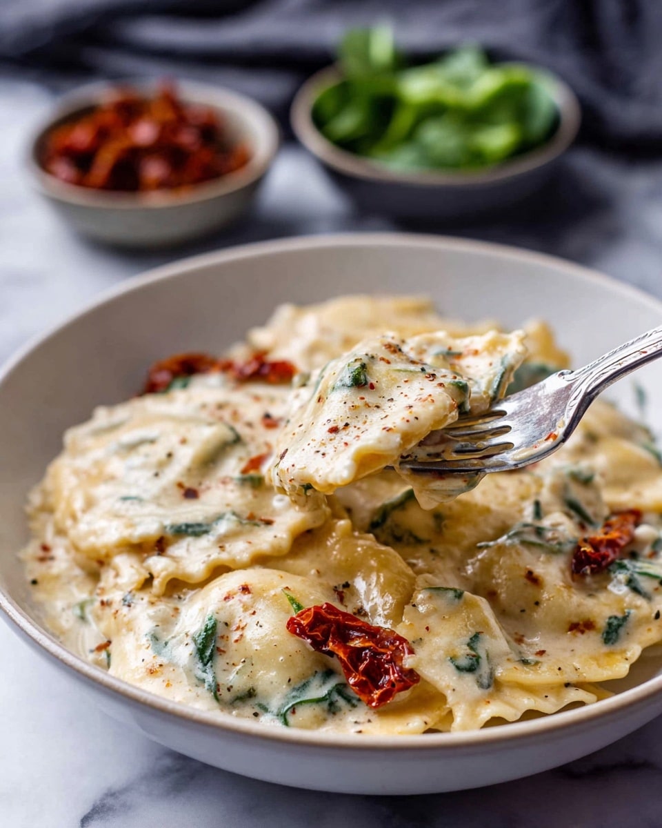 A white bowl holds about six large ravioli covered in a thick, creamy white sauce with visible specks of black pepper and bits of green spinach and small red sun-dried tomatoes scattered throughout. A silver fork is lifting one ravioli showing its soft, slightly golden edges and the creamy sauce clinging to it. In the blurred background, two small bowls sit on a white marbled surface, one with green leafy vegetables and the other with red sun-dried tomatoes. photo taken with an iphone --ar 4:5 --v 7