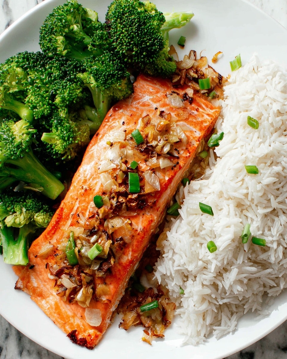A white plate holds three parts: at the top right, a pile of fluffy white rice with visible grains; below the rice, a large piece of cooked salmon with a bright orange color, topped with bits of browned garlic and chopped green onions scattered across its surface; at the bottom left, a bunch of vibrant green steamed broccoli florets arranged neatly. The plate sits on a white marbled surface. photo taken with an iphone --ar 4:5 --v 7