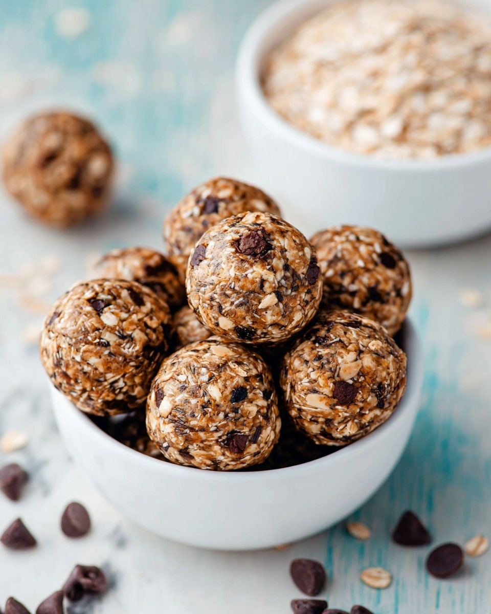 A white bowl filled with round energy balls made of oats, chia seeds, and small dark chocolate chips mixed evenly in a brownish base. Each ball is textured with visible oats and chocolate chips, showing a rough but compact surface. Near the bowl, small chocolate chips are scattered on a white marbled surface. In the background, another white bowl partially filled with oats is visible. The scene is bright and clean, with a soft focus on the background objects, photo taken with an iphone --ar 4:5 --v 7