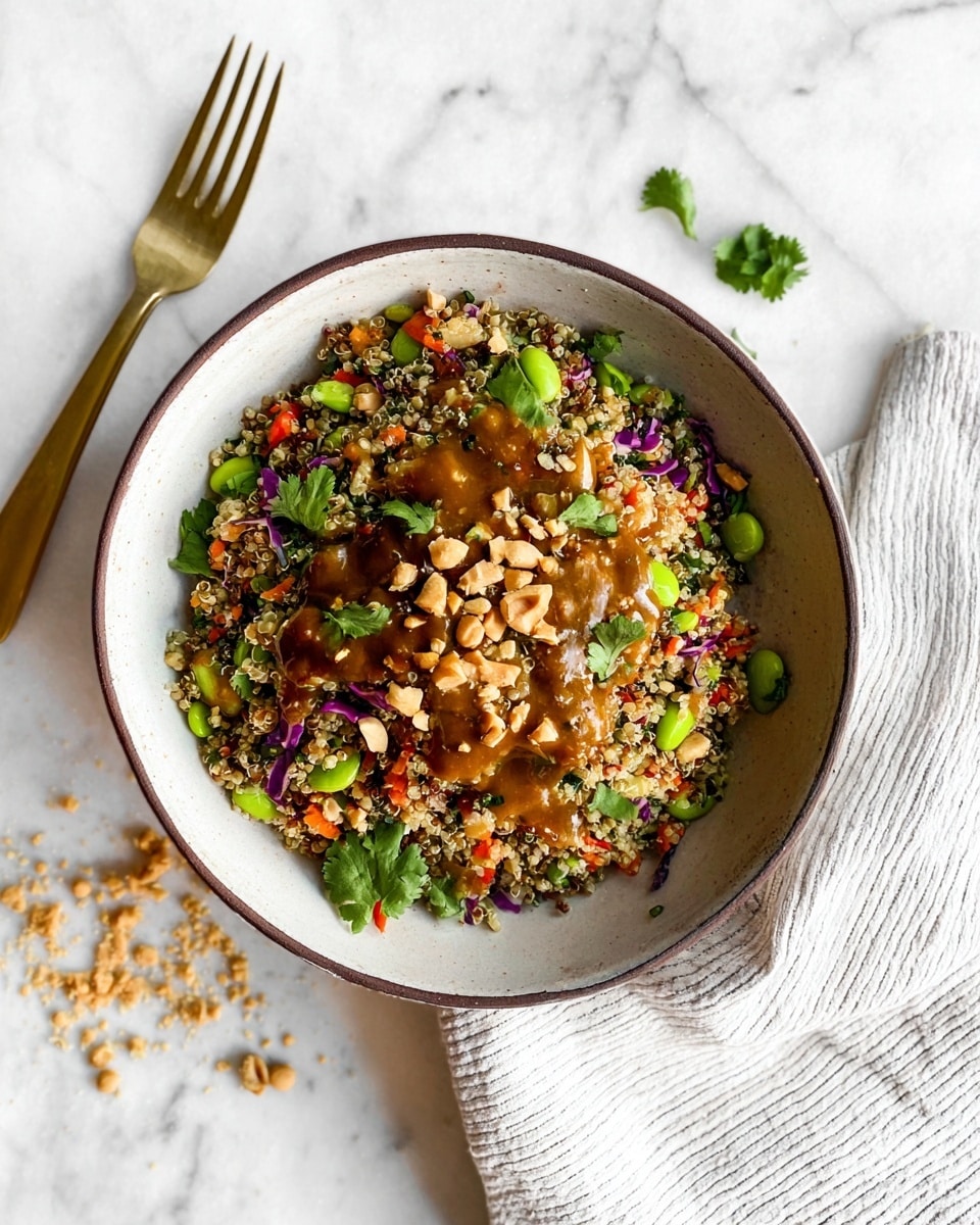 A bowl with a thin dark rim holds a colorful quinoa salad, layered with small beige quinoa grains mixed with green edamame, red bell pepper bits, and purple cabbage pieces. On top, a drizzle of brown sauce spreads unevenly with chopped peanuts and fresh green cilantro leaves scattered across. The bowl sits on a white marbled surface with peanut crumbs nearby, alongside a gold fork resting on a white striped cloth. Photo taken with an iphone --ar 4:5 --v 7