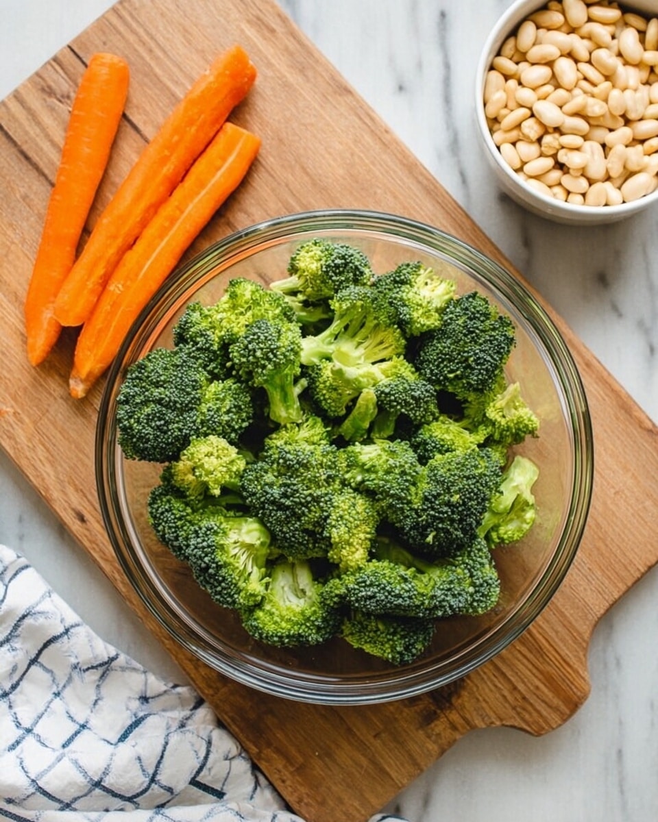 A clear glass bowl filled with bright green broccoli florets sits at the center on a wooden cutting board, which rests on a white marbled surface. Three whole orange carrots lie to the left of the bowl on the cutting board. To the top right of the bowl, there is a small white bowl filled with pale beige beans, placed on a white and blue striped cloth. The scene has soft, natural light. photo taken with an iphone --ar 4:5 --v 7