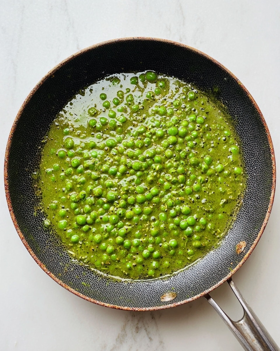 A black frying pan with a honeycomb patterned surface holds a green curry sauce mixed with bright green peas. The sauce is thick and textured with small bits, while the peas spread out evenly throughout, giving a dotted look. The pan's rim is slightly worn with a rusty brown color. The whole scene is set on a white marbled surface, with the metal handle of the pan visible on the bottom right. photo taken with an iphone --ar 4:5 --v 7