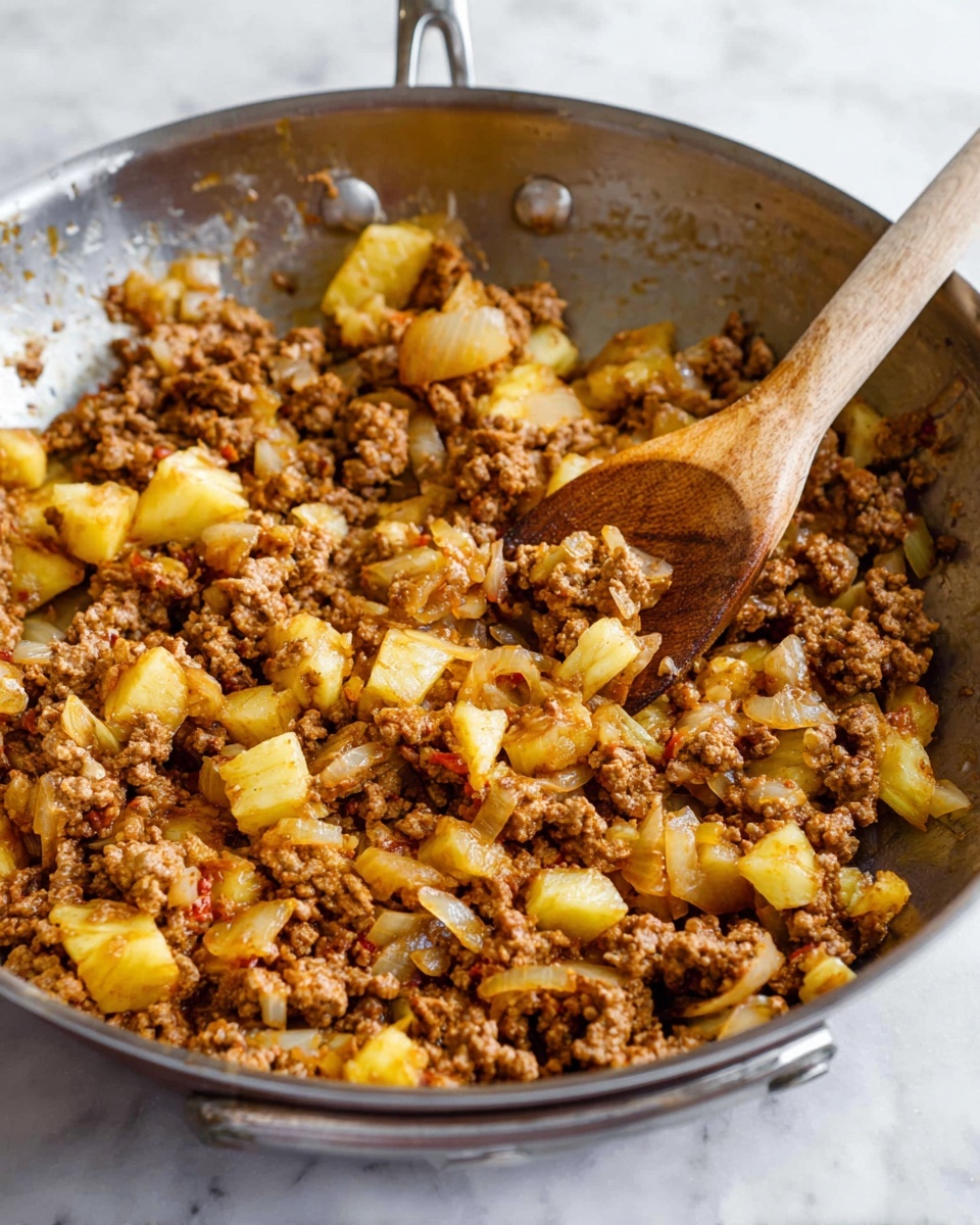 A close-up view of a metal pan filled with cooked ground meat mixed with visible pieces of diced yellow pineapple and translucent cooked onion chunks. The textures vary from crumbly brown meat to soft, slightly shiny onion slices and juicy pineapple bits. A wooden spoon with a long handle rests inside the pan, stirring the mixture over a white marbled surface. The pan edges and handles are visible around the food photo taken with an iphone --ar 4:5 --v 7