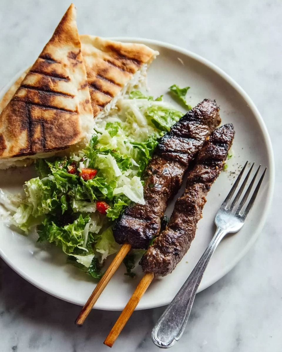 The dish shows a white plate with three main parts: a skewer of grilled dark brown meat with visible char marks placed on the right side, a folded triangular piece of grilled flatbread with dark brown grill lines on the left side, and a small portion of green leafy lettuce mixed with small bits of red vegetables in the center near the flatbread. A silver fork lies on the right edge of the plate next to the skewer. The plate sits on a white marbled surface. Photo taken with an iphone --ar 4:5 --v 7