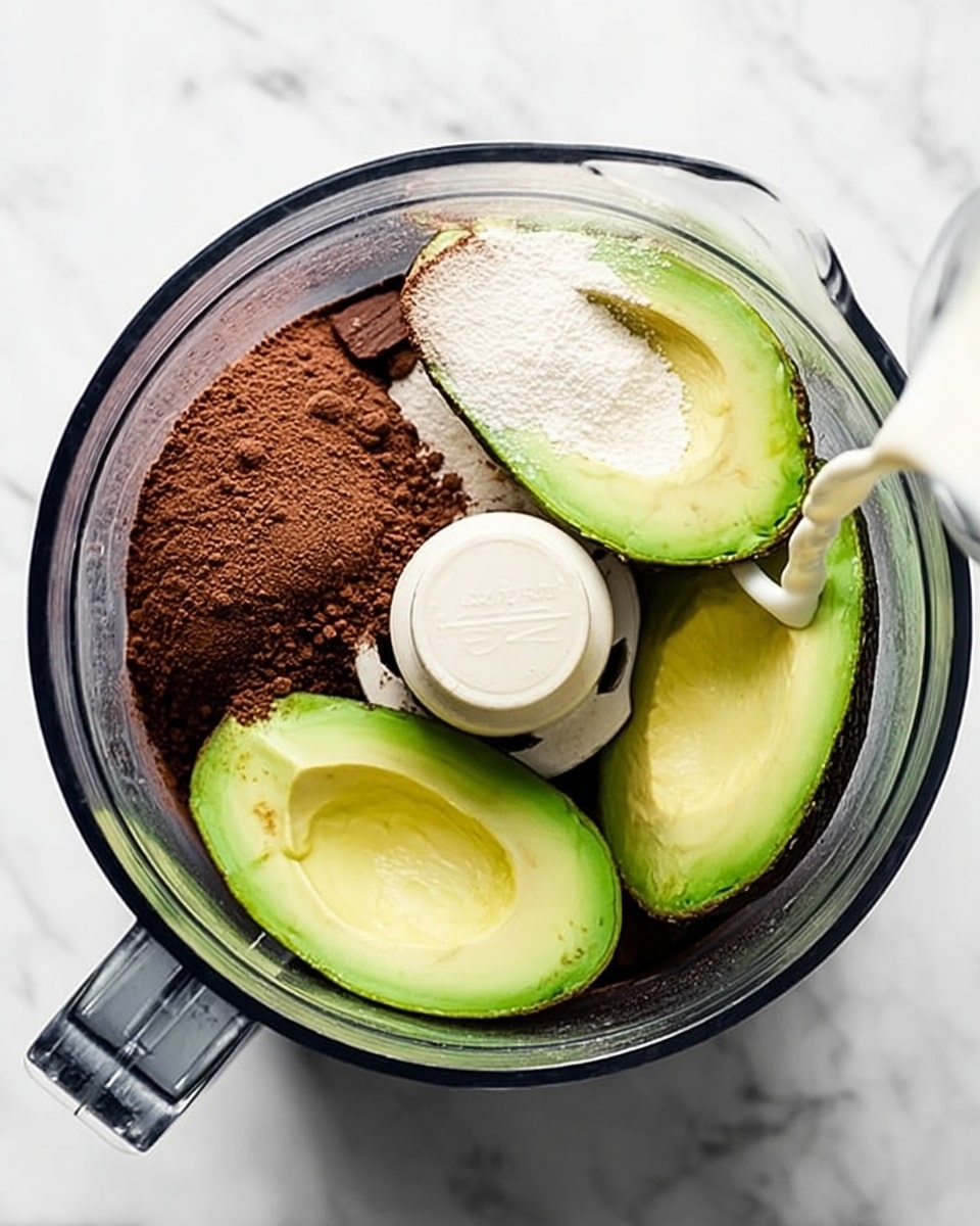 The image shows a top view of a blender bowl on a white marbled surface filled with three green avocado halves with smooth creamy textures and dark green skins, two piles of dark brown cocoa powder with powdery textures, and a pour of white liquid from a clear glass cup into the bowl, creating a contrast of colors and textures. The blender's white plastic blade system is centered among the ingredients. photo taken with an iphone --ar 4:5 --v 7