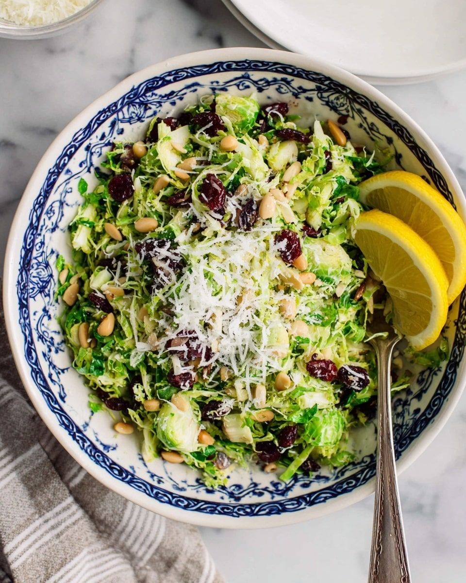 A white bowl with blue patterns holds a salad made of shredded bright green Brussels sprouts as the base layer, topped with scattered light brown pine nuts and dark red dried cranberries. There is a generous sprinkle of finely grated white cheese spread across the top, with two fresh lemon slices placed on one side. A silver spoon is partially inside the bowl on the right side. The bowl is placed on a white marbled surface with a striped cloth in the corner, and a white plate is partially visible nearby. Photo taken with an iphone --ar 4:5 --v 7