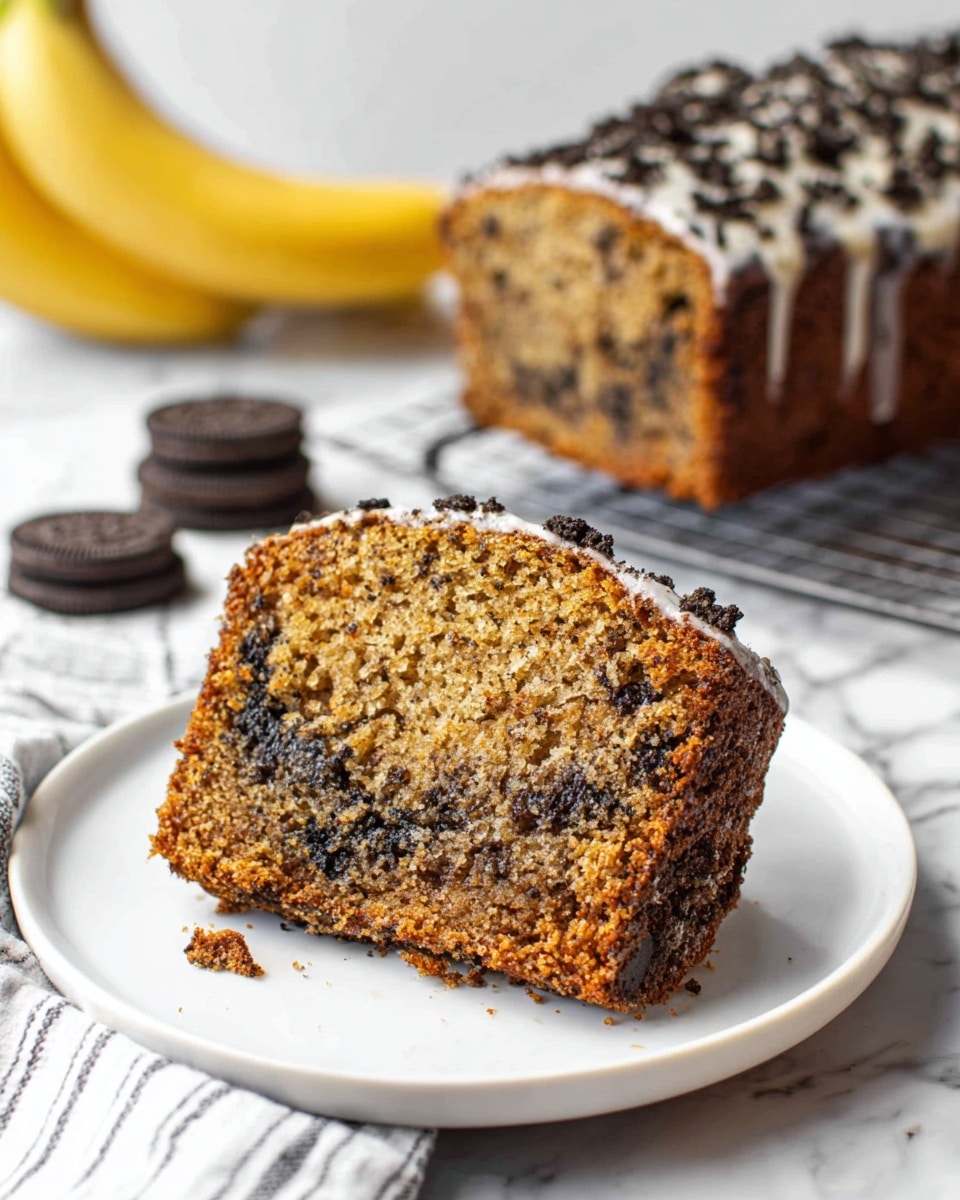A thick slice of moist banana cake sits on a white plate, showing a light brown crumb with dark chocolate pieces mixed inside. The edges have a rough texture with bits of crushed cookies and a thin layer of white frosting clinging to the sides. In the background, a larger loaf of the same cake topped with crushed cookies is placed on a cooling rack, with a couple of whole chocolate sandwich cookies and a banana nearby on a white marbled surface. A white and gray striped cloth partly appears on the left side. Photo taken with an iphone --ar 4:5 --v 7
