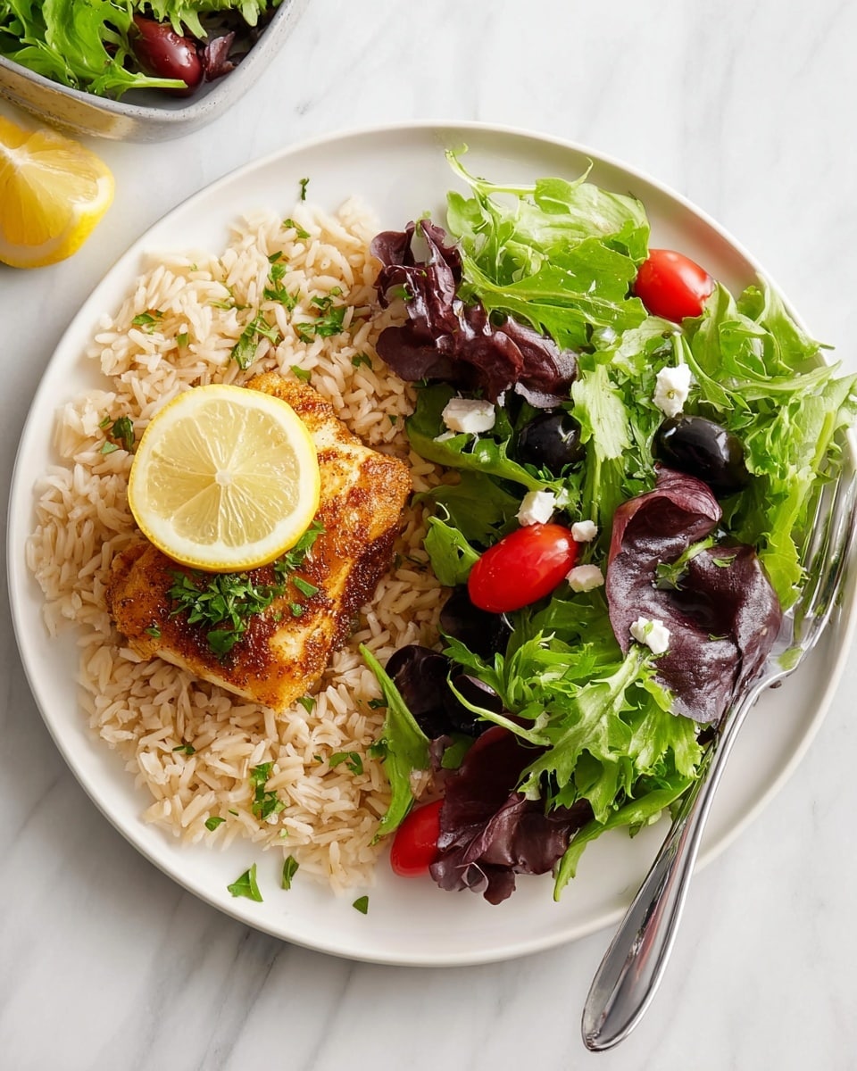 A white round plate sits on a white marbled surface, holding three main layers: a base of light brown cooked rice sprinkled with small green herb pieces, a middle layer of golden-brown cooked fish fillet with a slightly crispy texture topped with a thin lemon slice, and a fresh salad on the side composed of dark purple and bright green leafy greens mixed with shiny red grape tomatoes, dark olives, and small white cheese crumbles. A silver fork lies next to the plate. Photo taken with an iphone --ar 4:5 --v 7