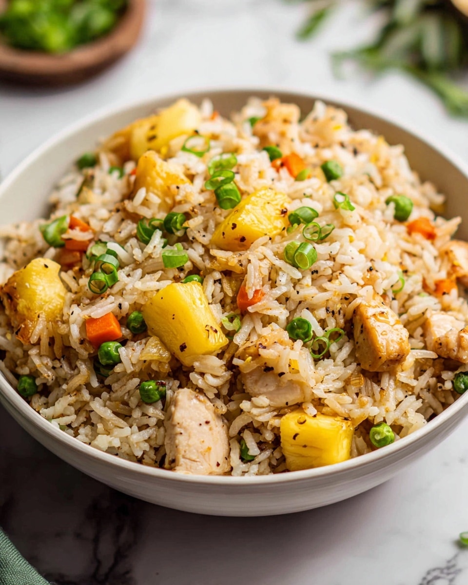 A close-up view of a bowl filled with fried rice, showing about five layers of mixed ingredients. The base is white rice, speckled with black pepper and light brown seasoning. Mixed in are bright yellow pieces of pineapple, light green peas, small bits of orange carrots, and chunks of light beige cooked chicken. The top layer is garnished with chopped dark green spring onions. The bowl is white and set on a white marbled surface, with some blurred greenery in the background. photo taken with an iphone --ar 4:5 --v 7
