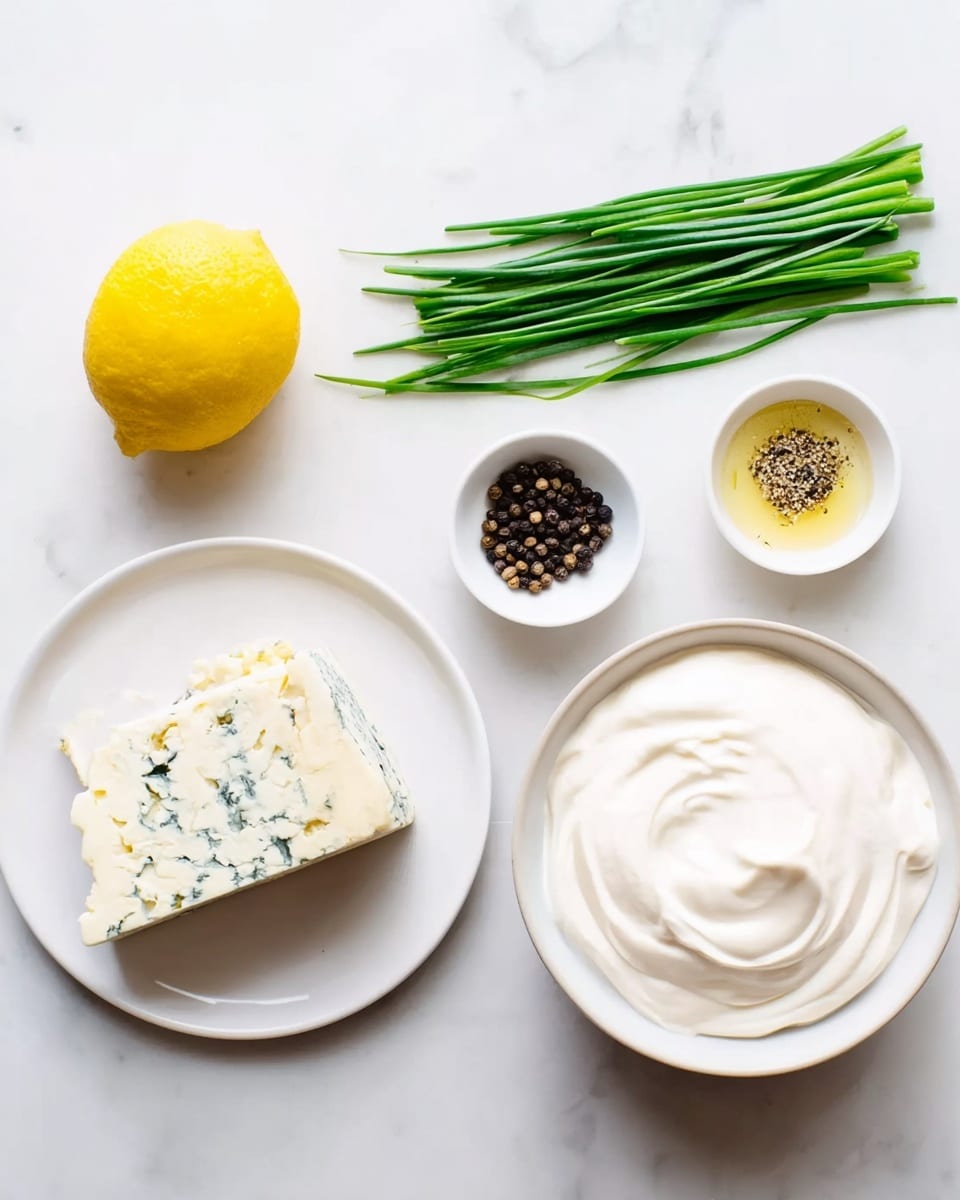 The image shows an overhead view of several ingredients on a white marbled surface. There is a white plate with a block of blue cheese featuring light yellow and blue-green mold areas on one side. Next to this is a small bunch of fresh green chives laid out in a parallel arrangement. A whole yellow lemon is placed nearby. There are two small white bowls, one filled with a swirl of creamy white sauce, and the other containing whole black peppercorns. In the center, there is a large white bowl filled with thick white creamy yogurt or sour cream with smooth texture. The setup is neat and bright, with a simple, clean aesthetic. photo taken with an iphone --ar 4:5 --v 7