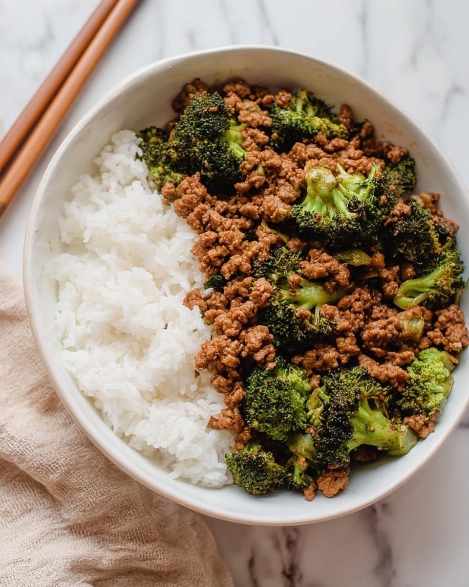 A white bowl filled with two main layers: on the left side, fluffy white rice with a soft texture, and on the right side, cooked ground meat mixed with bright green broccoli florets. The meat has a slightly moist, crumbly texture and is spread evenly among the broccoli pieces. The bowl sits on a white marbled surface with a part of a beige cloth and wooden chopsticks visible in the background. photo taken with an iphone --ar 4:5 --v 7