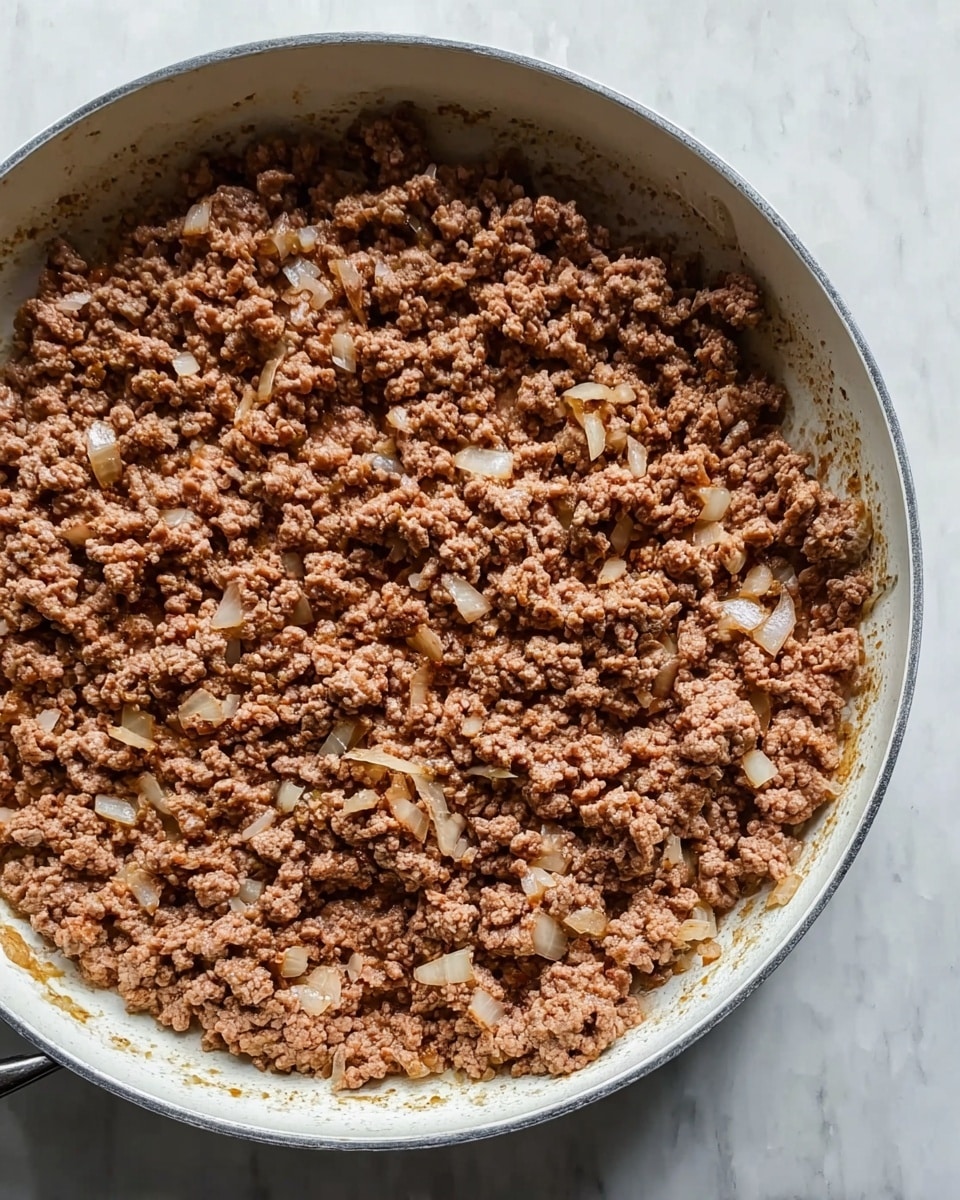 A close-up view of a white pan filled with cooked ground meat mixed with small pieces of soft, translucent onion evenly spread across the surface. The meat is brown with a crumbly texture, and the pan sits on a white marbled surface. Photo taken with an iphone --ar 4:5 --v 7