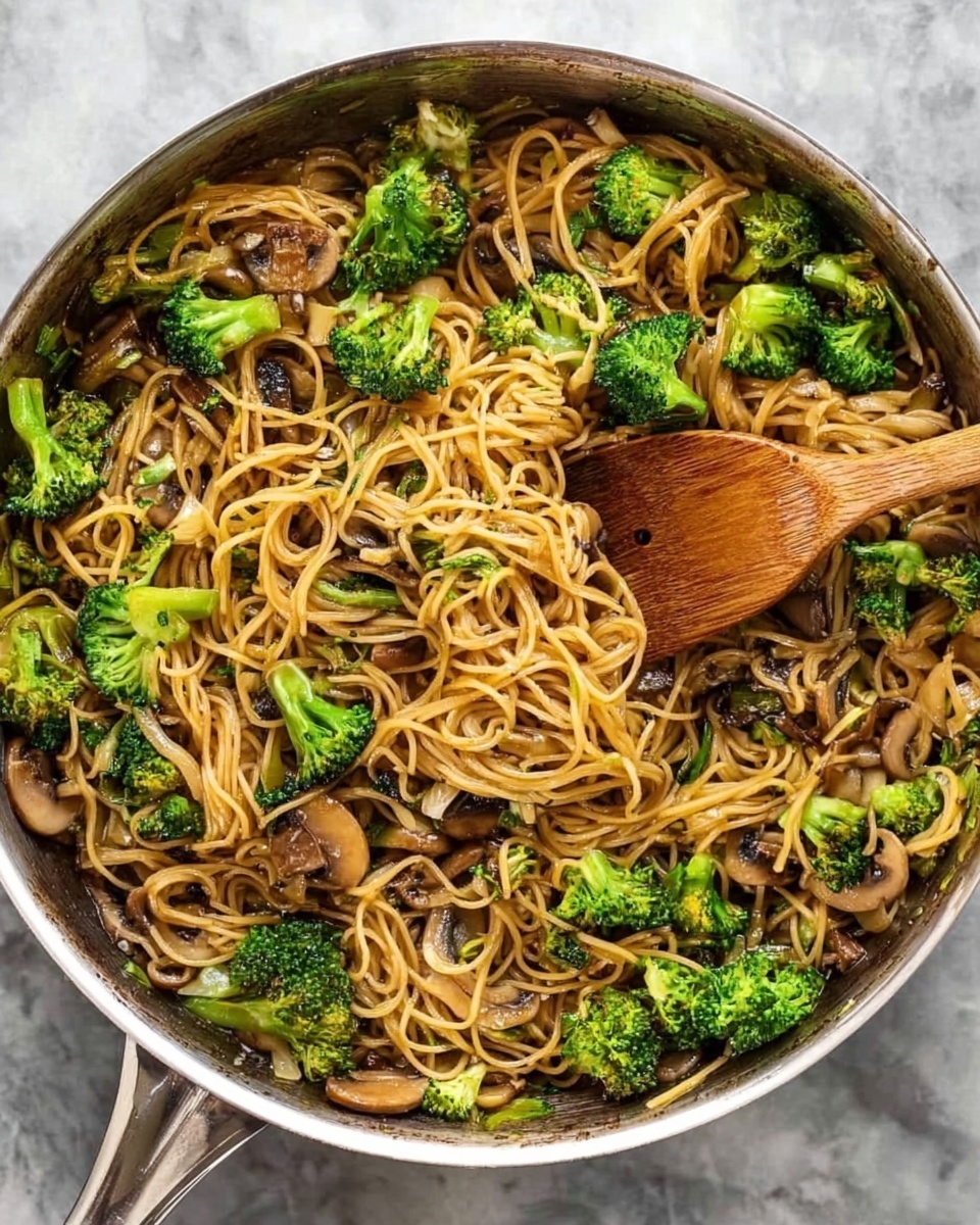 The image shows a close-up of a pan filled with stir-fried noodles mixed with green broccoli florets and light brown mushroom slices. The noodles are golden-brown with a slightly shiny texture, tangled together evenly throughout the pan. The bright green broccoli pieces are scattered all over, adding a fresh look, while the mushrooms are thinly sliced and mixed well with the noodles and broccoli. A wooden spatula is placed in the pan, slightly lifting some noodles and vegetables. The pan sits on a white marbled surface. Photo taken with an iphone --ar 4:5 --v 7