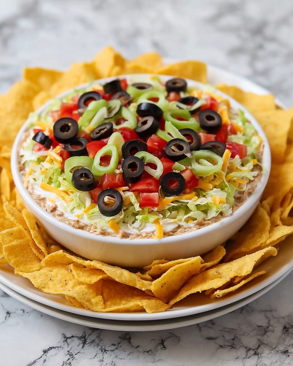 A white bowl filled with a layered dip sits in the center of a white plate. The bottom layer appears creamy and light brown. On top of it is a thin green layer of shredded lettuce, followed by a layer of shredded yellow and white cheese scattered evenly. Red diced tomatoes and chopped light green bell peppers are spread over the cheese. Black olive rings cover the top, creating a colorful contrast. Surrounding the bowl on the white plate are yellow corn chips, creating a border around the bowl. The whole set is placed on a white marbled surface. photo taken with an iphone --ar 4:5 --v 7
