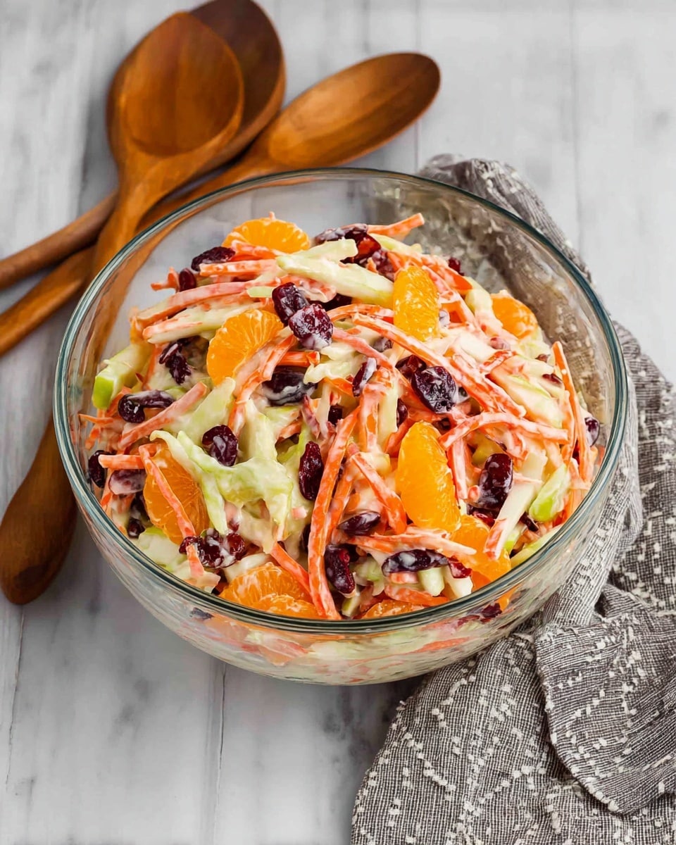 A clear glass bowl sits on a white marbled surface, filled with a colorful salad made of multiple layers. The bottom and middle layers show thin orange carrot sticks mixed with light green apple slices that have red edges, creating a crisp texture. There are also bright orange mandarin orange segments scattered throughout, adding a juicy, soft layer. Dark red dried cranberries are mixed inside, giving a chewy texture and a splash of contrast. The entire salad is coated lightly with a creamy, pale dressing that adds a smooth finish to the mix. Around the bowl are wooden salad spoons and a gray cloth with a subtle pattern. photo taken with an iphone --ar 4:5 --v 7