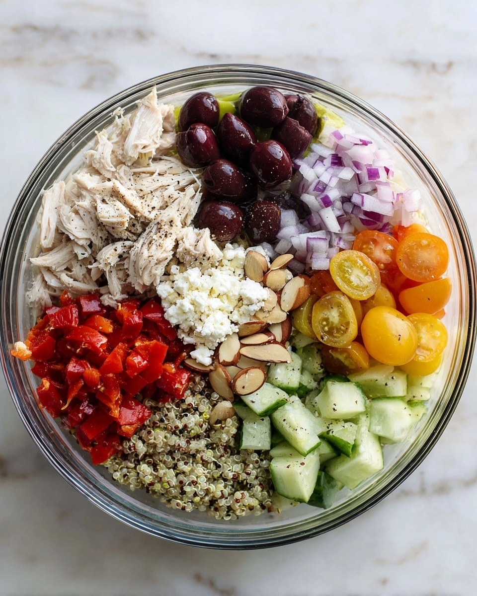 A clear glass bowl holds a colorful layered salad, placed on a white marbled surface. Starting from the top left, there is a layer of shredded white chicken lightly sprinkled with black pepper, next to dark purple halved olives. Below the olives, bright red and orange cherry tomatoes sliced in half create a vibrant cluster. Just below the tomatoes is a mix of white and red quinoa grains. Moving clockwise, pale green cucumber chunks sprinkled with black pepper fill the bowl’s bottom right. Above the cucumber, toasted sliced almonds add a light brown crunchy texture. Near the middle, a small mound of white crumbled cheese is placed in the center. To the left of the cheese is a pile of diced red roasted peppers and finely chopped purple onions complete the bowl’s colorful layers. Photo taken with an iphone --ar 4:5 --v 7