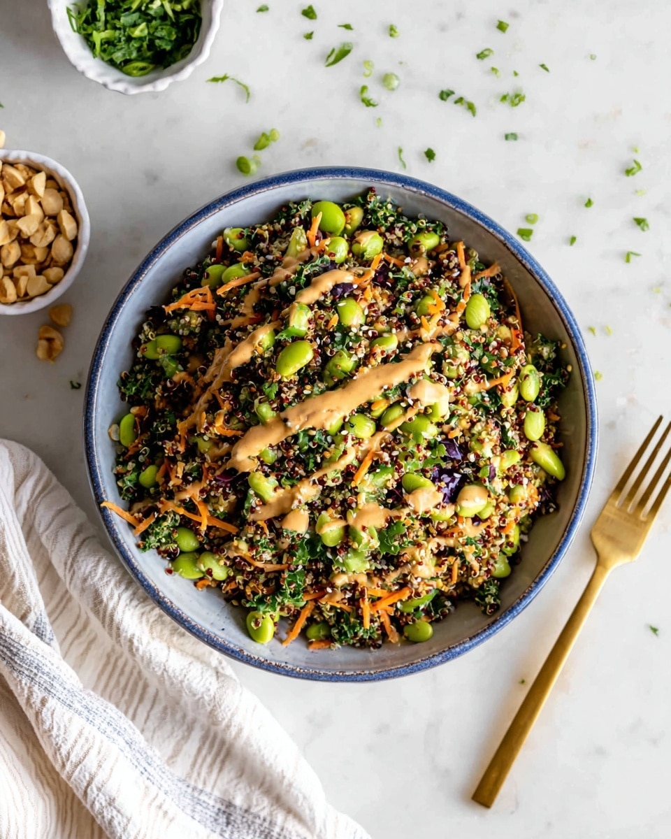 A bowl with a blue rim filled with a colorful quinoa salad that has green edamame beans, orange shredded carrots, chopped green onions, dark leafy greens, and small white sesame seeds mixed throughout. The salad is topped with a light brown, creamy dressing drizzled over the top. The bowl sits on a white marbled surface scattered with chopped green herbs and some small nuts. A small white bowl with chopped green herbs and a golden fork lie nearby. A white cloth with thin stripes is partially visible near the bottom left corner of the image. photo taken with an iphone --ar 4:5 --v 7